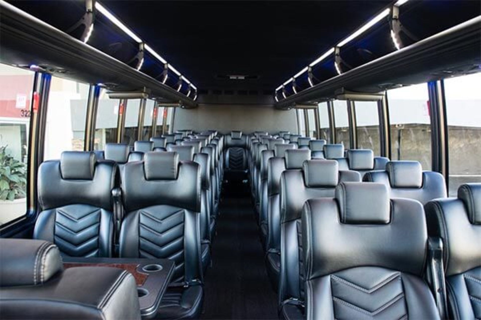 Interior of a black coach bus with rows of black leather seats. Overhead storage compartments run the length of the bus.