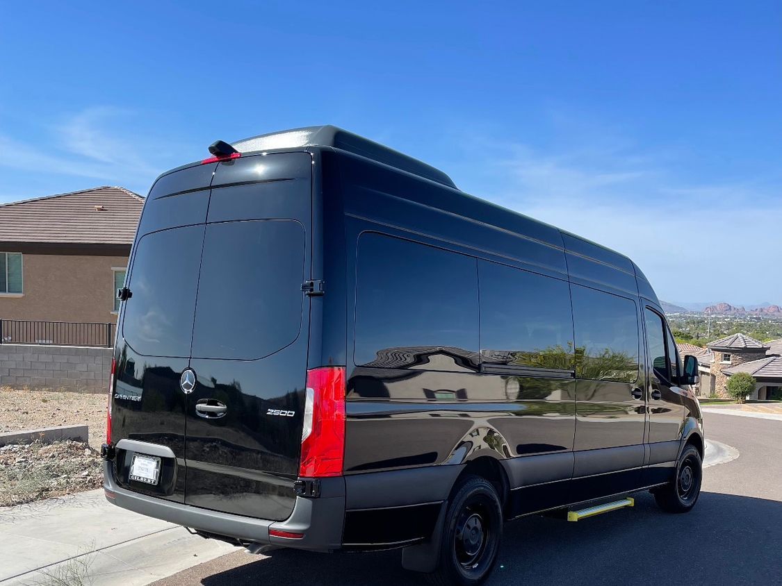 Black passenger van parked on a residential street on a sunny day. The van has tinted windows and a running board.