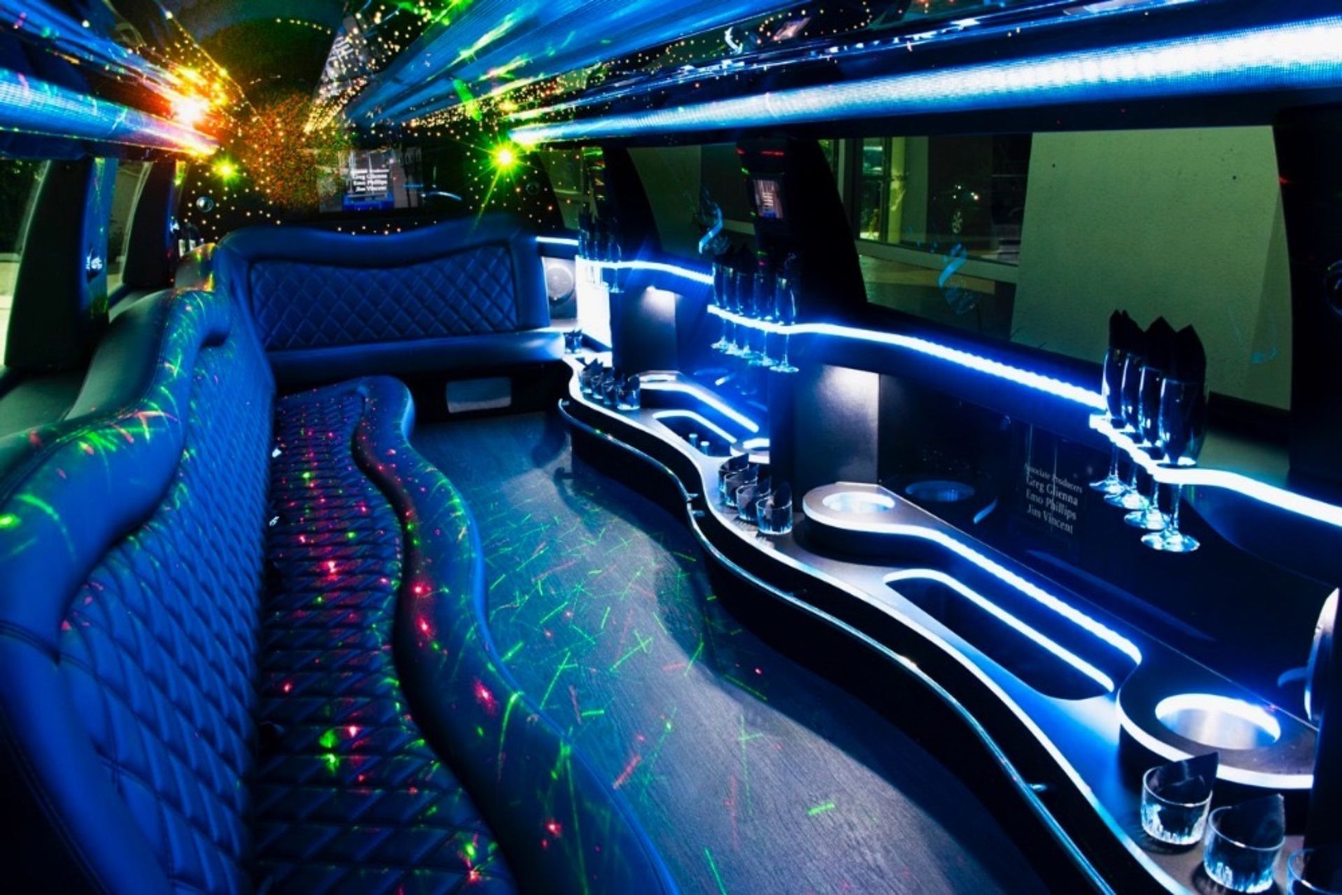 Inside of a limousine with blue and multi-colored LED lights illuminating the interior, bar, and seating.