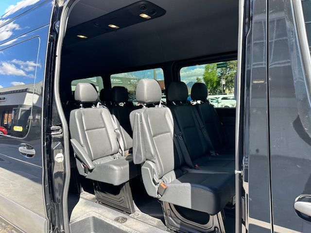 Interior of a black van with rows of black seats. The side door is open, revealing seats for passengers.