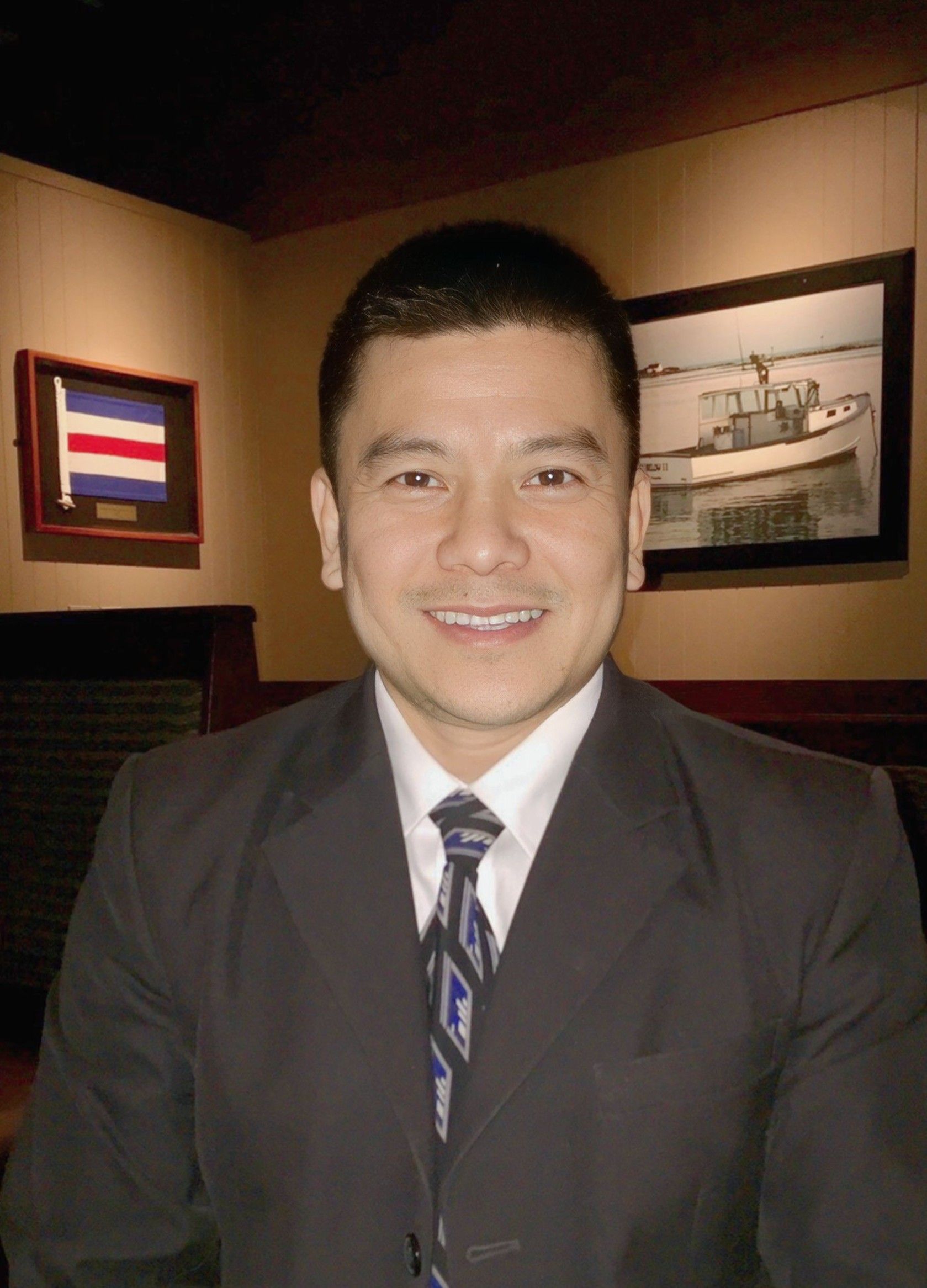 Man in suit smiling at the camera, indoors, with artwork on the wall behind him.