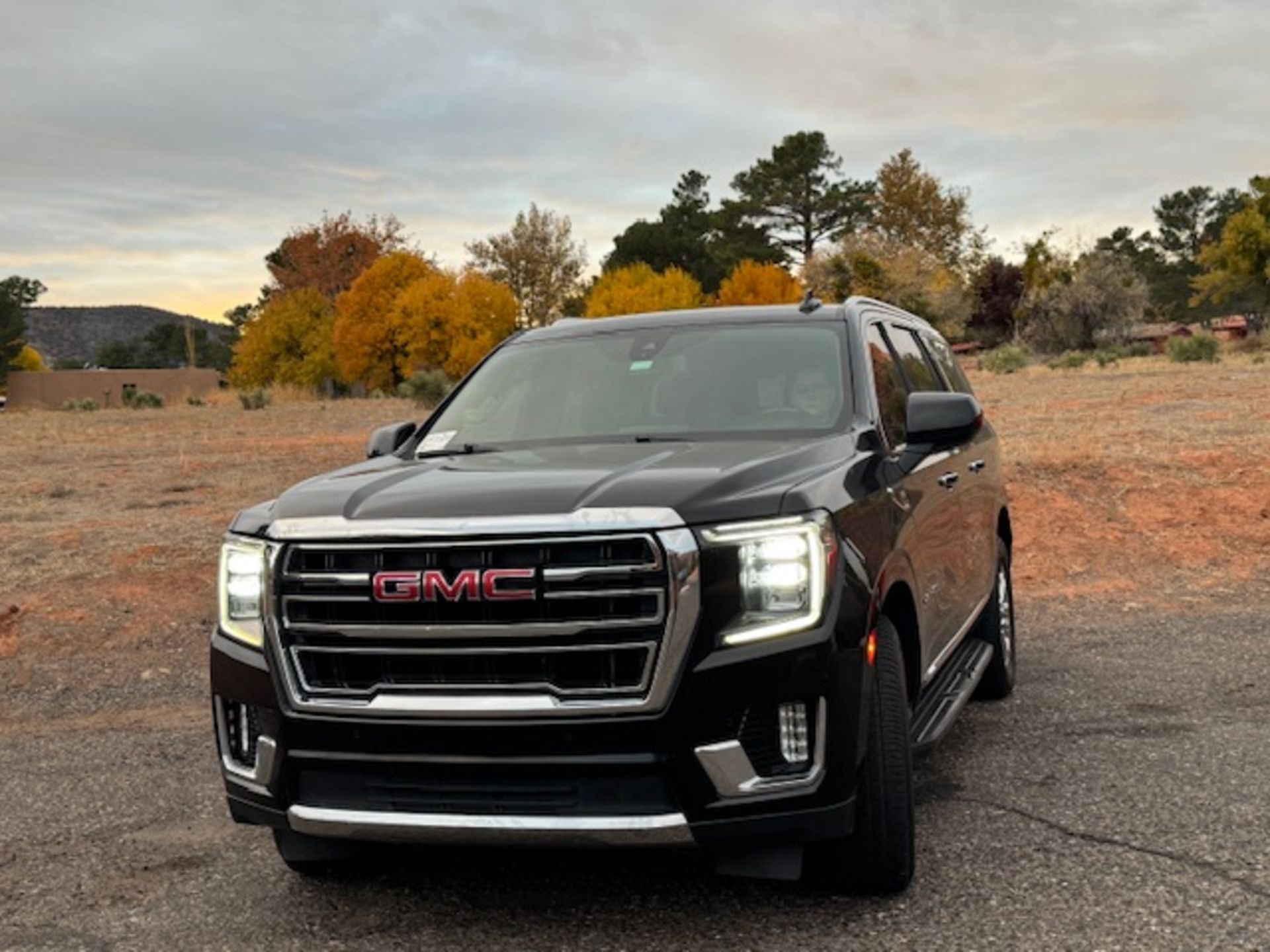 Black GMC Yukon SUV parked outdoors on a paved area with fall foliage and a cloudy sky.