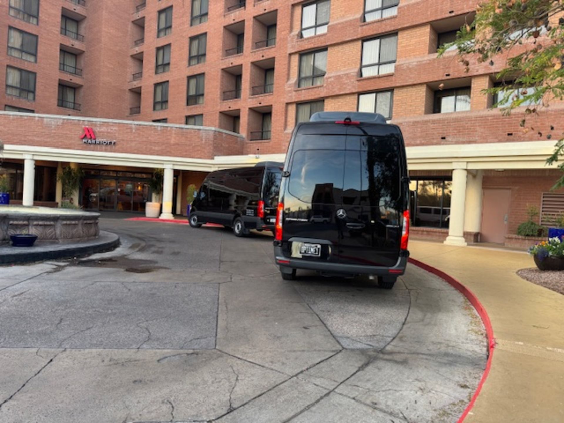 Black vans parked in front of a Marriott hotel with a red brick facade. Entrance under a covered awning.