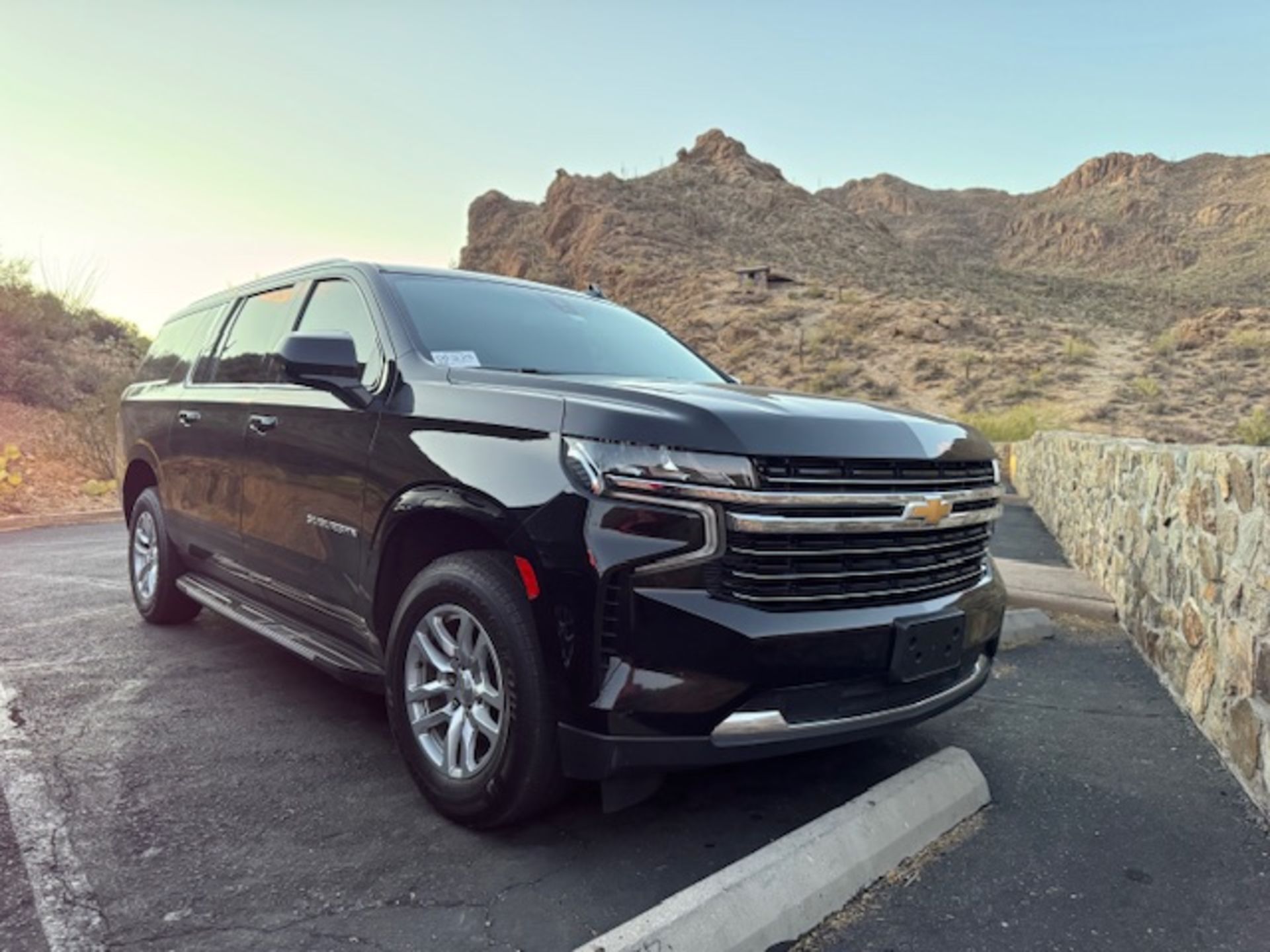 Black SUV parked near a stone wall and a mountain backdrop. Evening light.