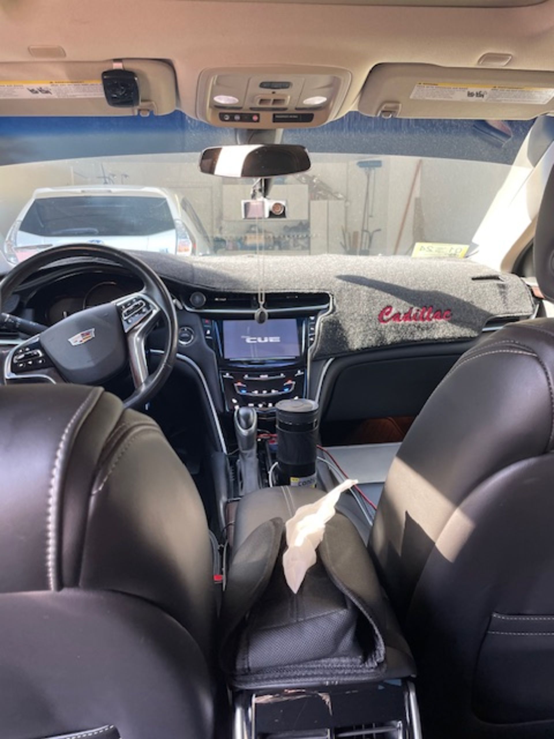 Interior view of a Cadillac car. The dashboard and seats are black, with a car wash visible through the windshield.