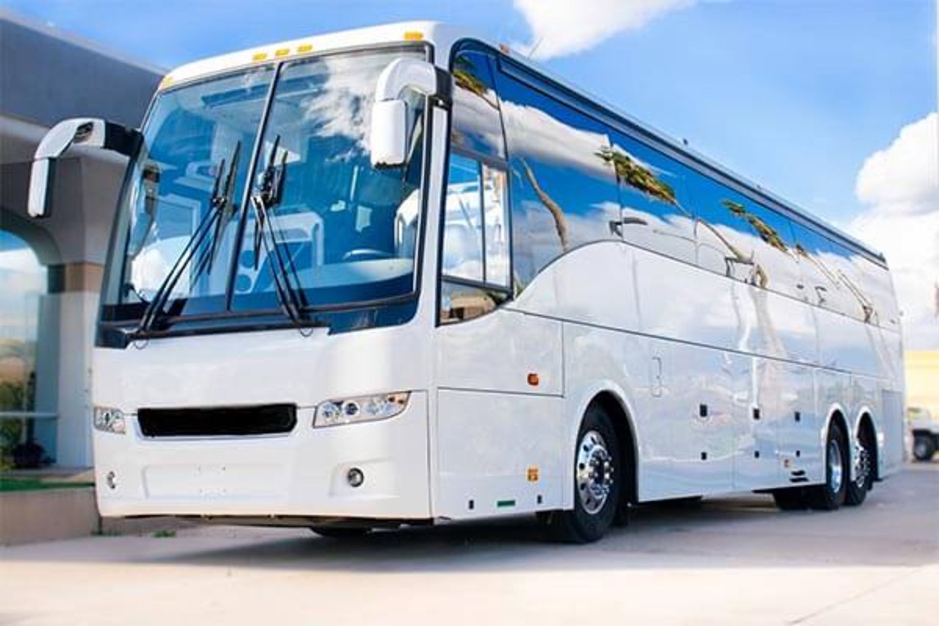 White charter bus parked near a building; blue sky reflected in its windows.