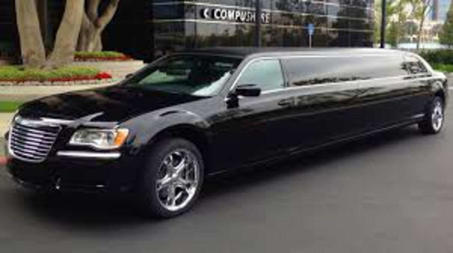 Black Chrysler 300 limousine parked on a street in front of a modern building.