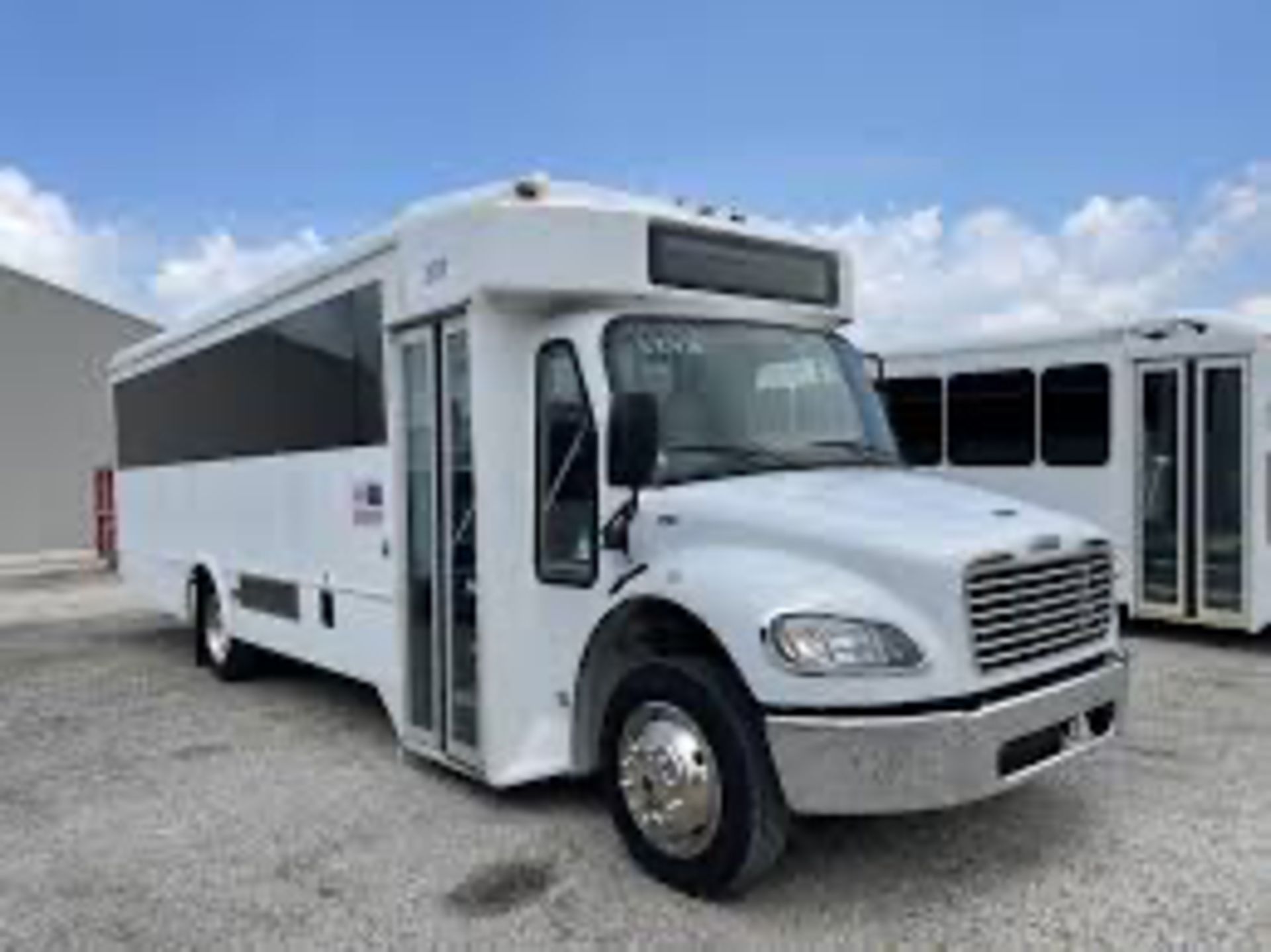 White bus parked on a concrete surface, likely for transporting people. The bus has tinted windows and a front door.