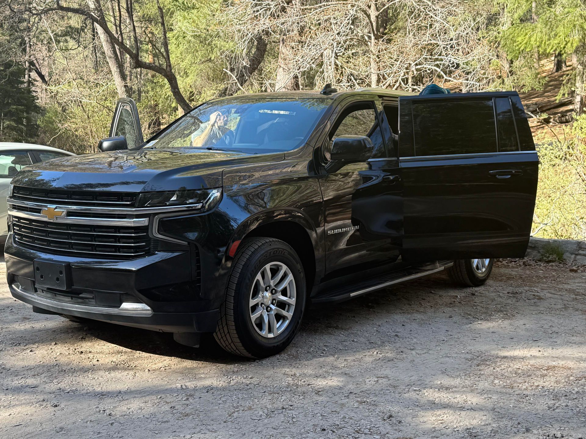 Black Chevrolet SUV parked on gravel with driver's side door open.  The setting is outdoors, trees visible in the background.