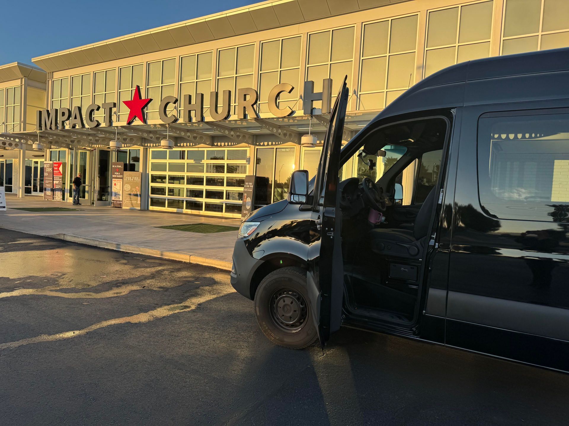 A black van parked in front of "Impact Church" with its door open. The building has a red star and glass garage doors.