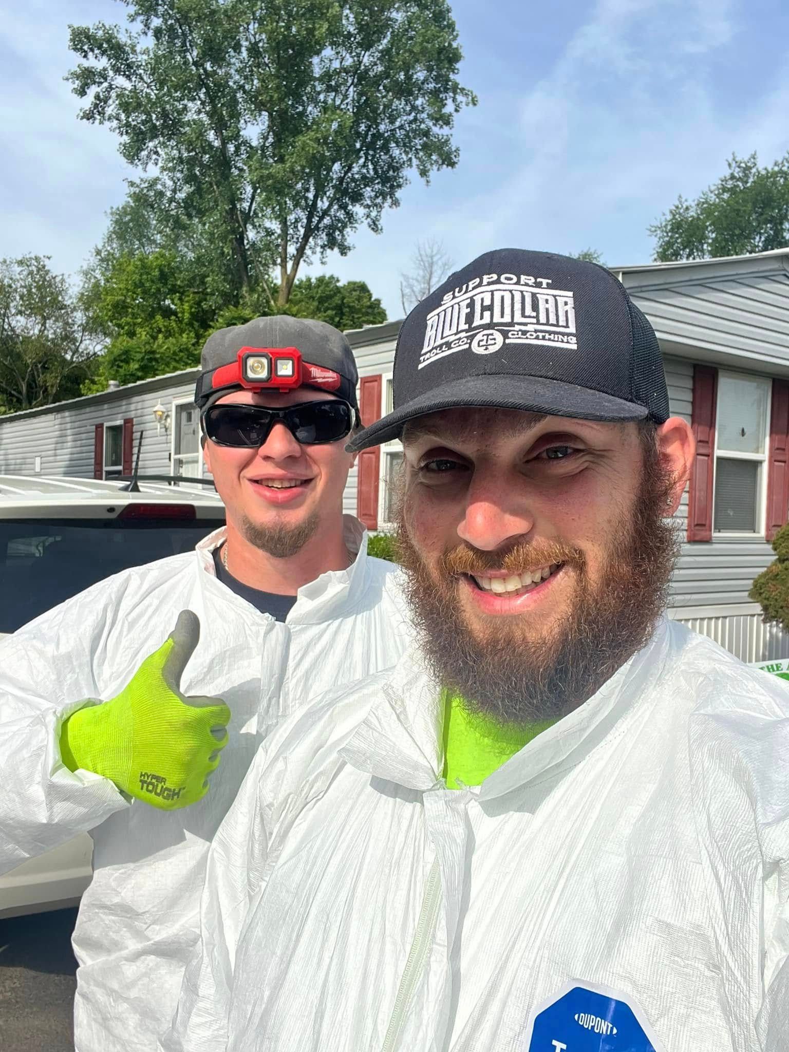 Two men wearing protective suits and hats are posing for a picture.