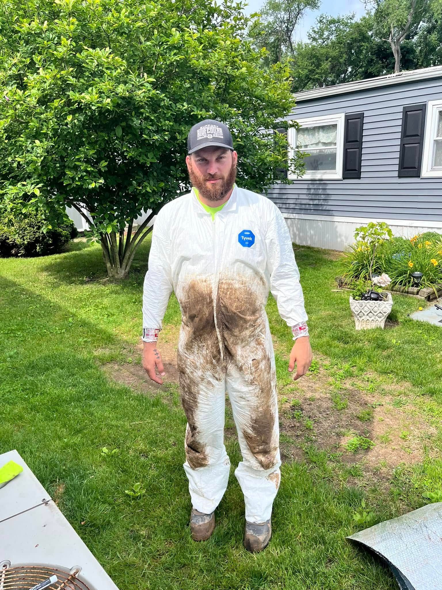 A man in a white coverall is standing in the grass in front of a house.