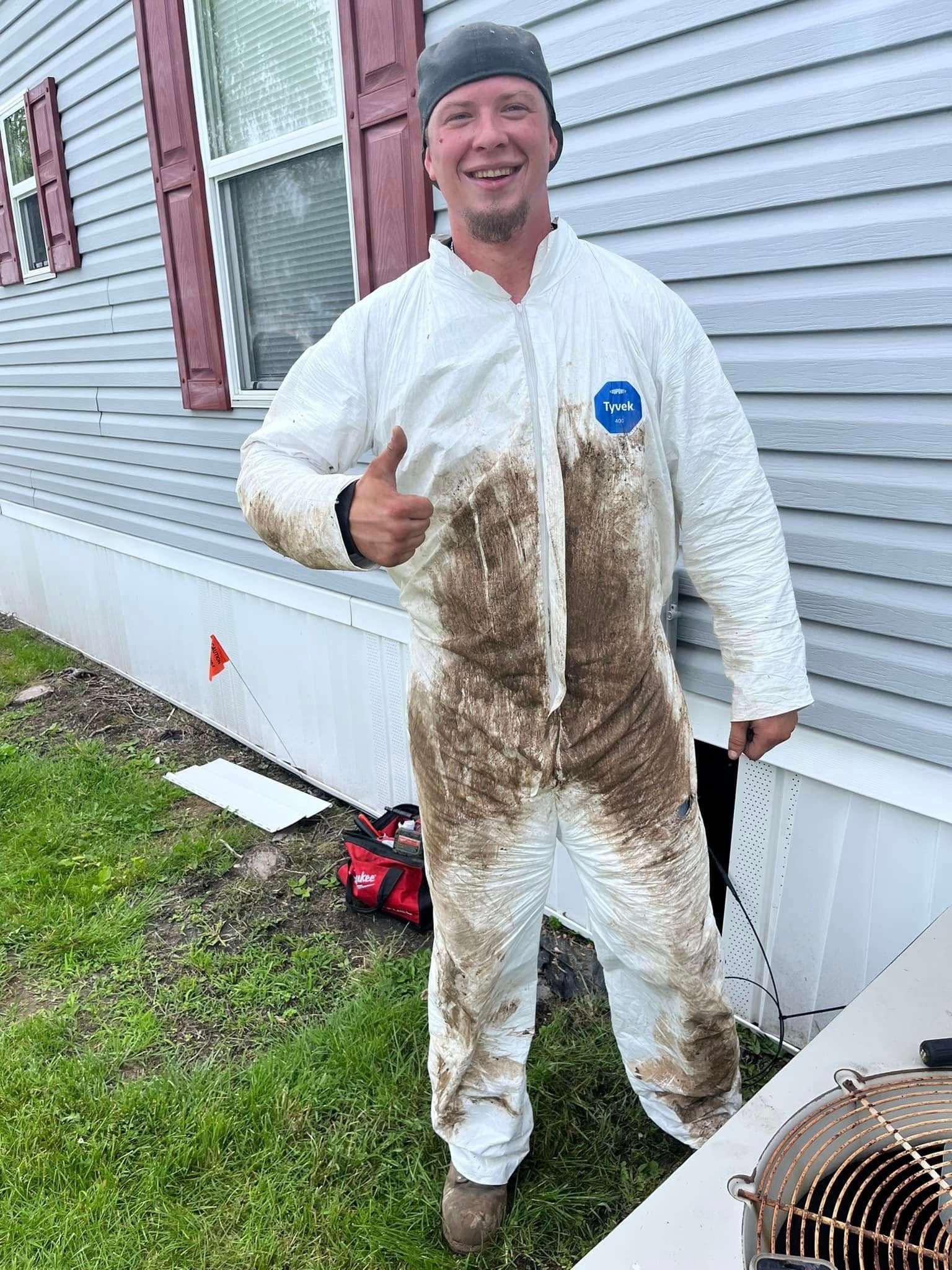 A man in a white coverall is standing in front of a house giving a thumbs up.