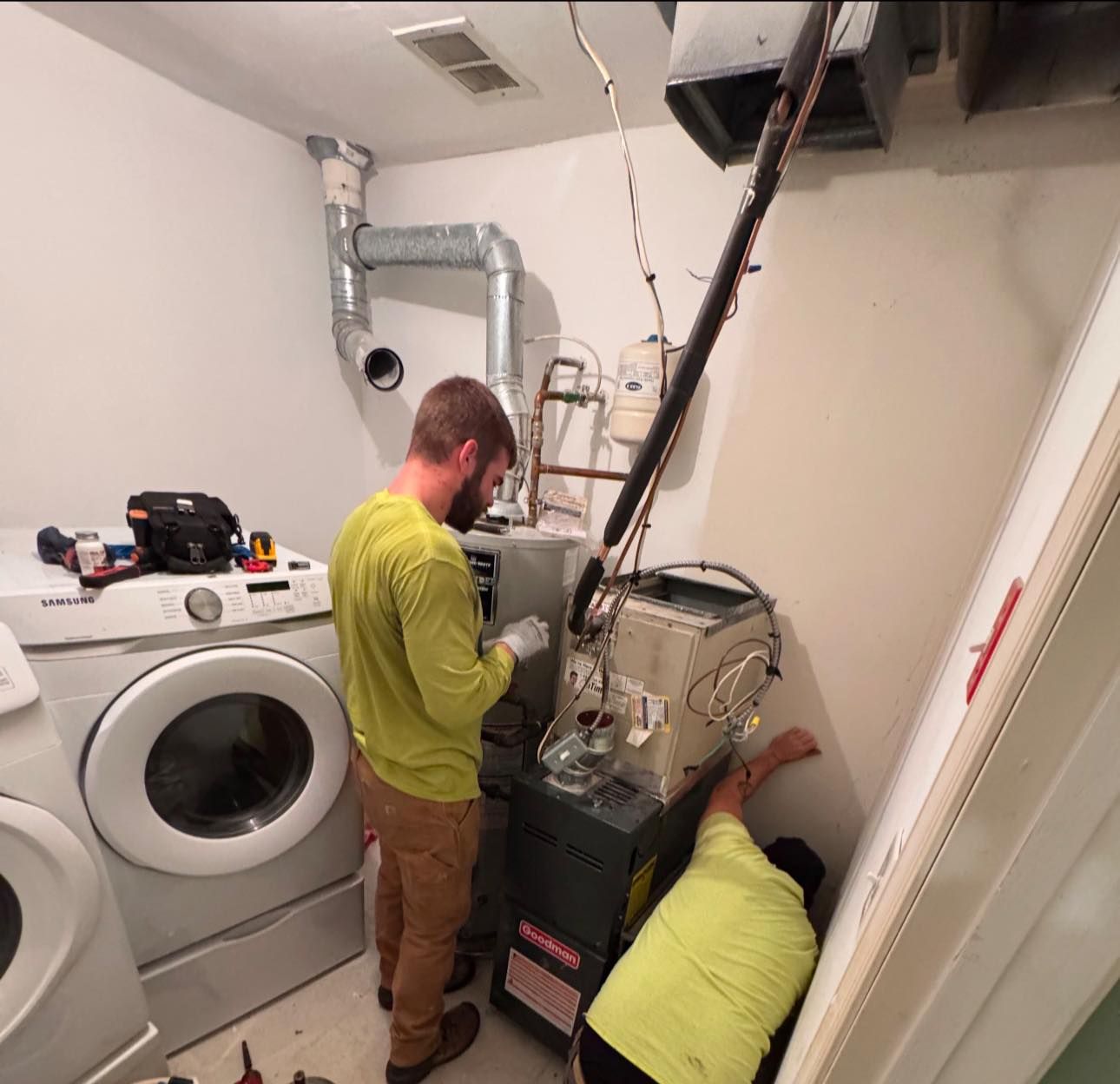 Two men are working on a washer and dryer in a laundry room