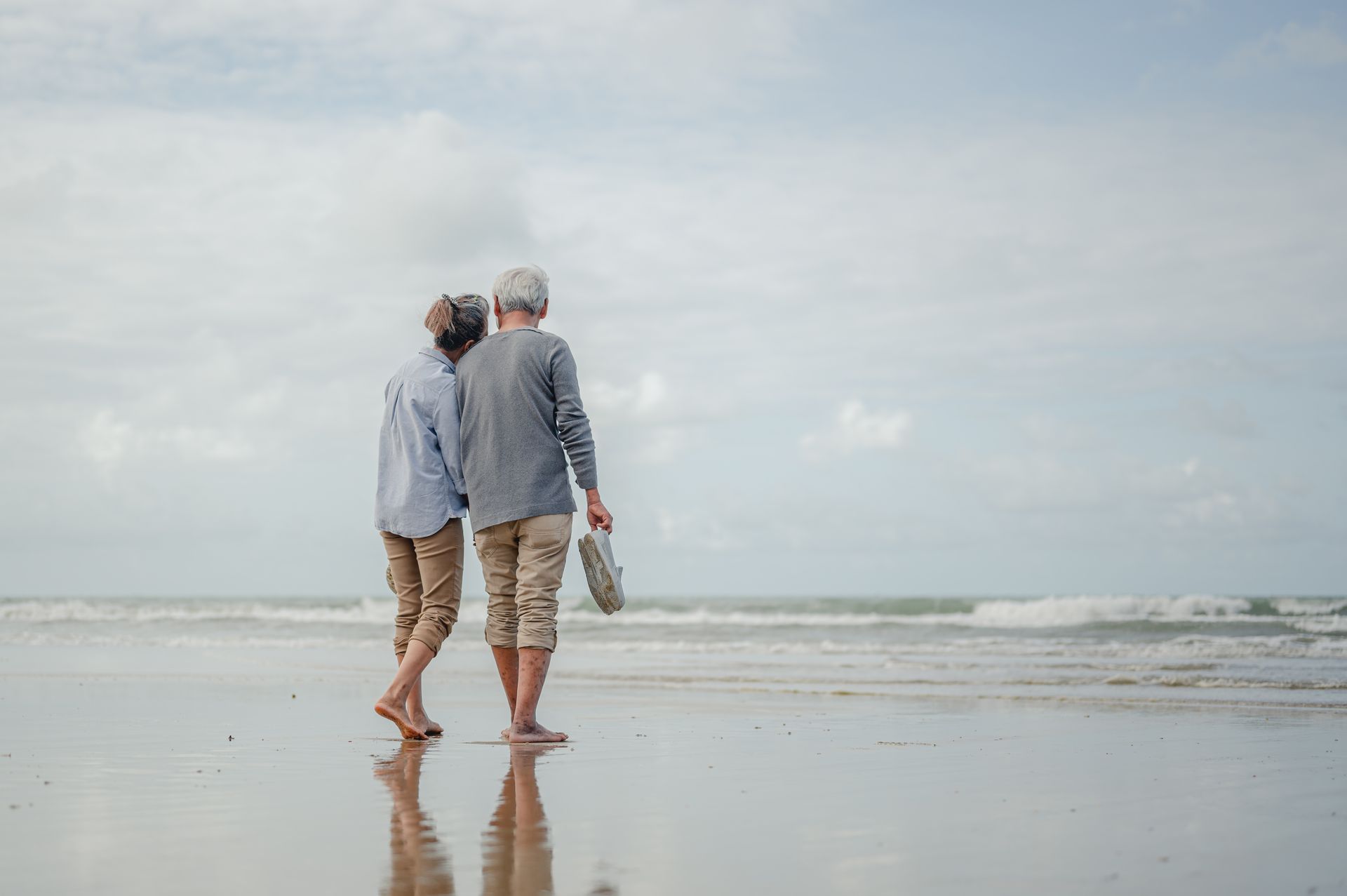 an elderly couple is walking on the beach .