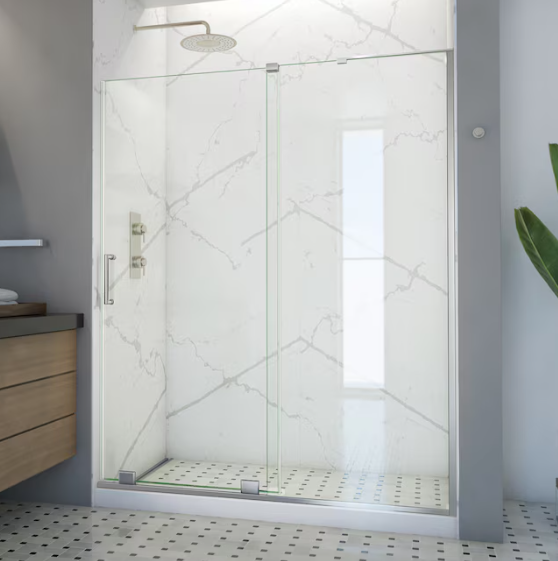 A glass shower enclosure with a chrome handle against a white marble-patterned wall inside a modern bathroom.