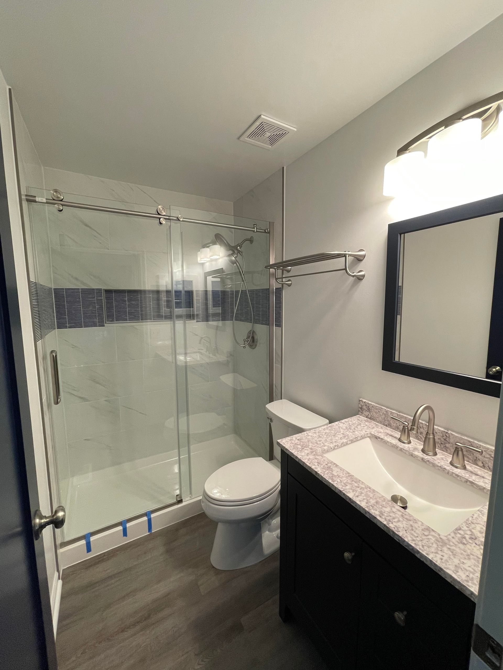 A bathroom with a toilet, sink, mirror and shower.