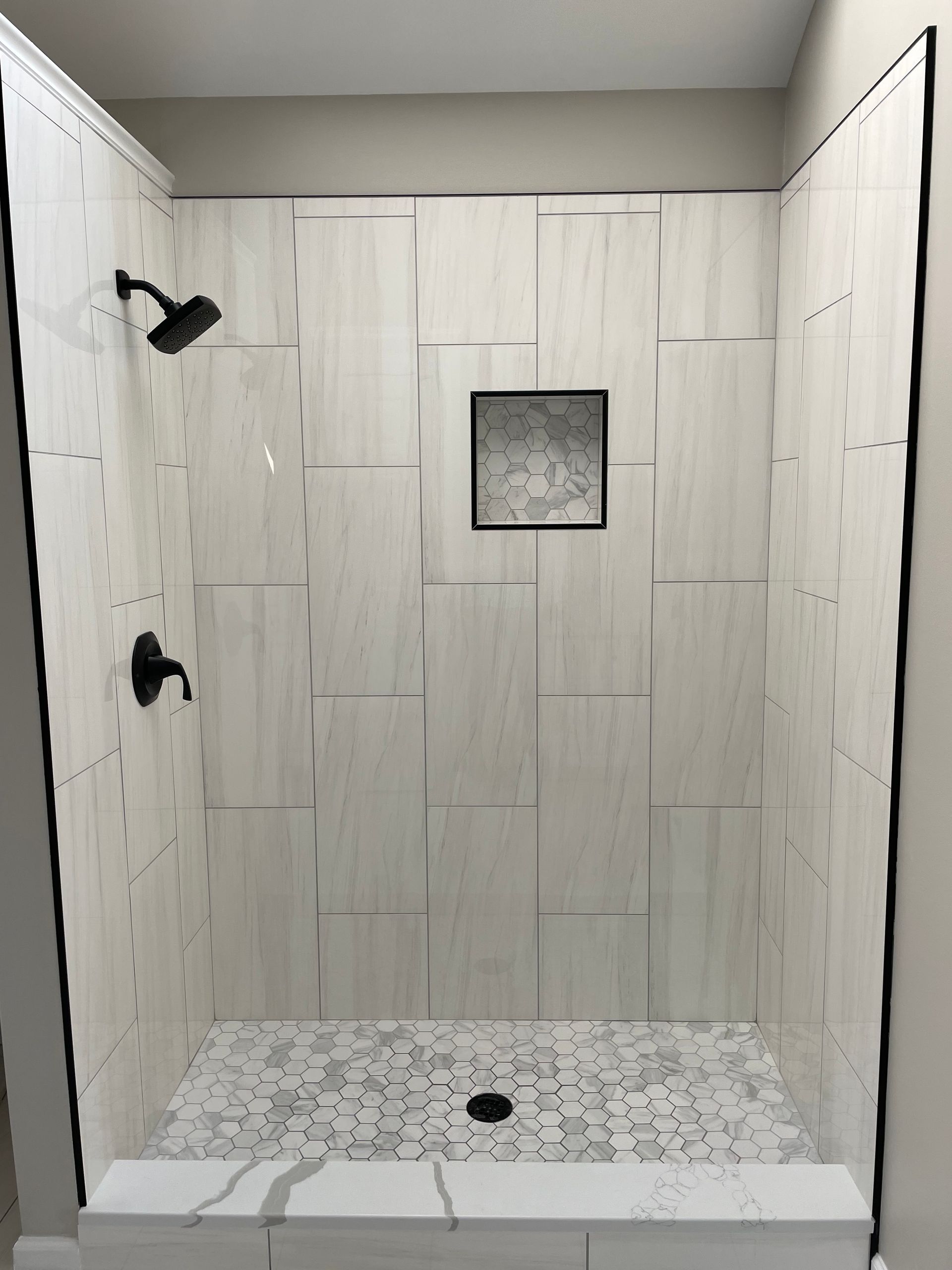 A shower stall with white tiles and a black shower head.