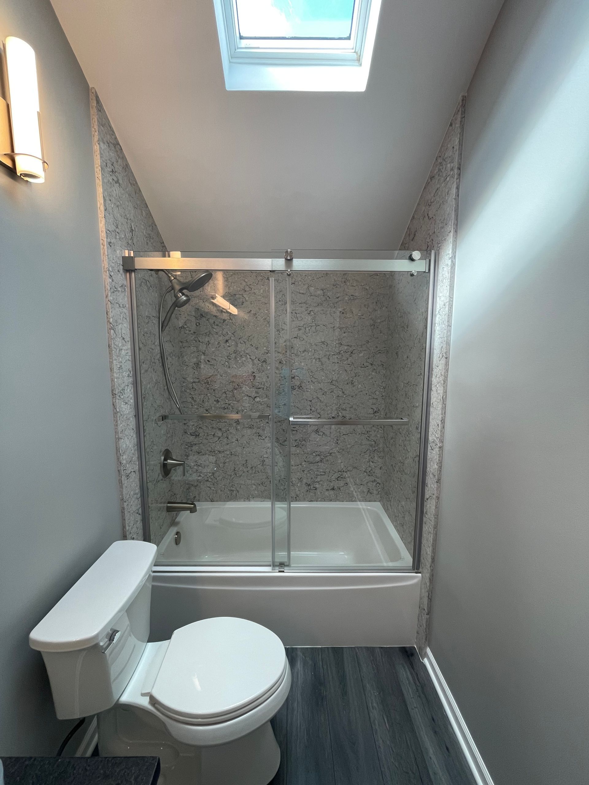 A bathroom with a toilet , tub , shower and skylight.