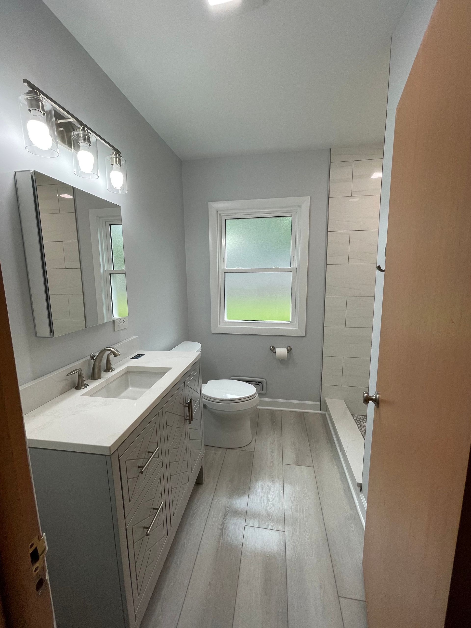 A bathroom with a sink , toilet , mirror and window.