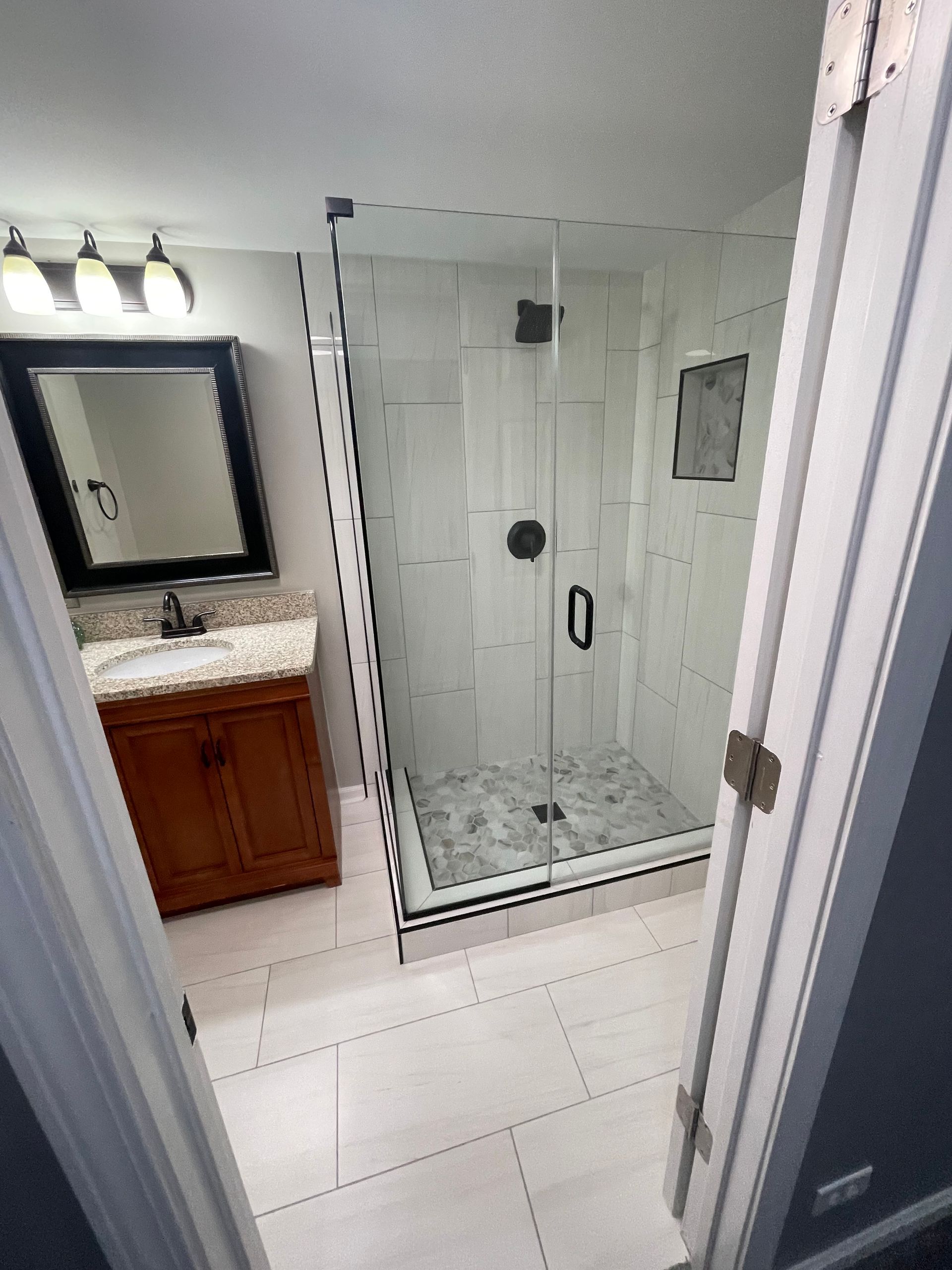 A bathroom with a walk in shower , sink and mirror.
