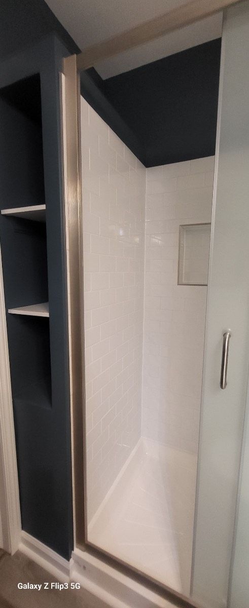 A bathroom with a walk in shower and shelves.