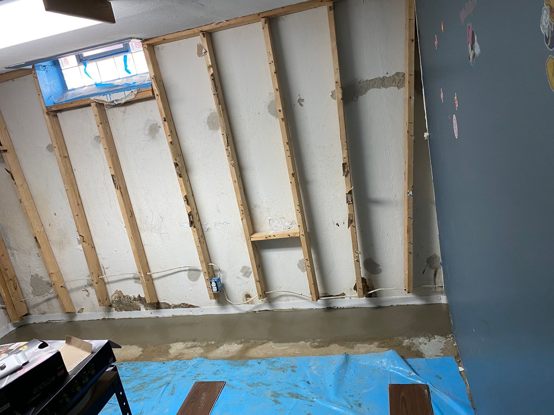Cracked concrete basement wall with gray patching. Wooden beams above.