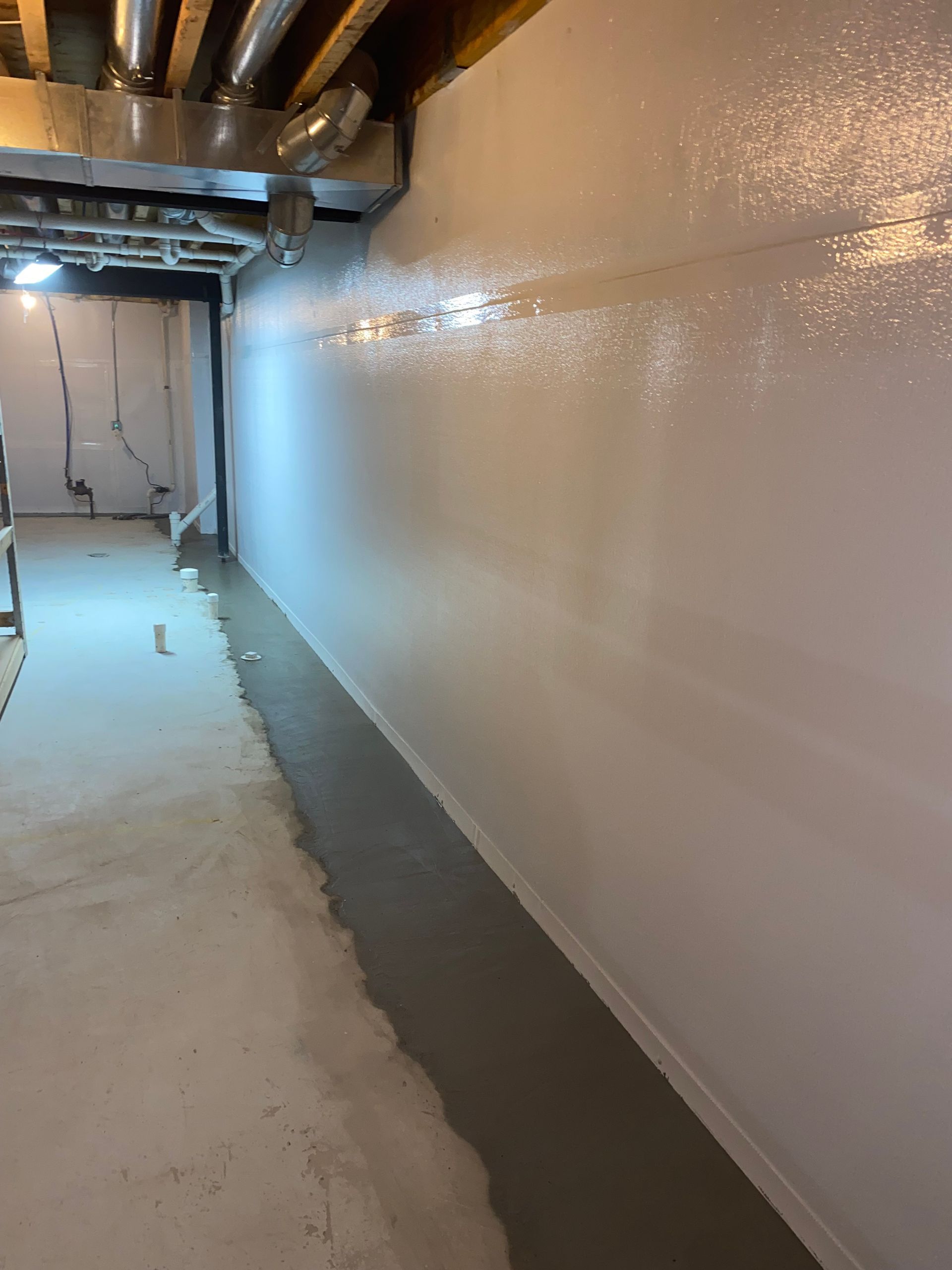 A sump pump system in a gray-painted basement, including a pump, piping, and a black backup power unit.