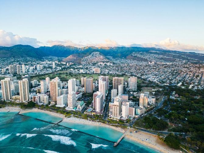 An aerial view of a city with a beach and mountains in the background.