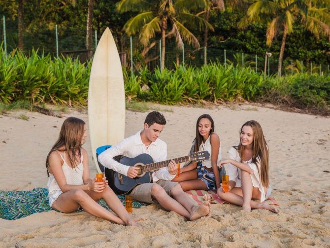 A group of people are sitting on the beach with a guitar and a surfboard.