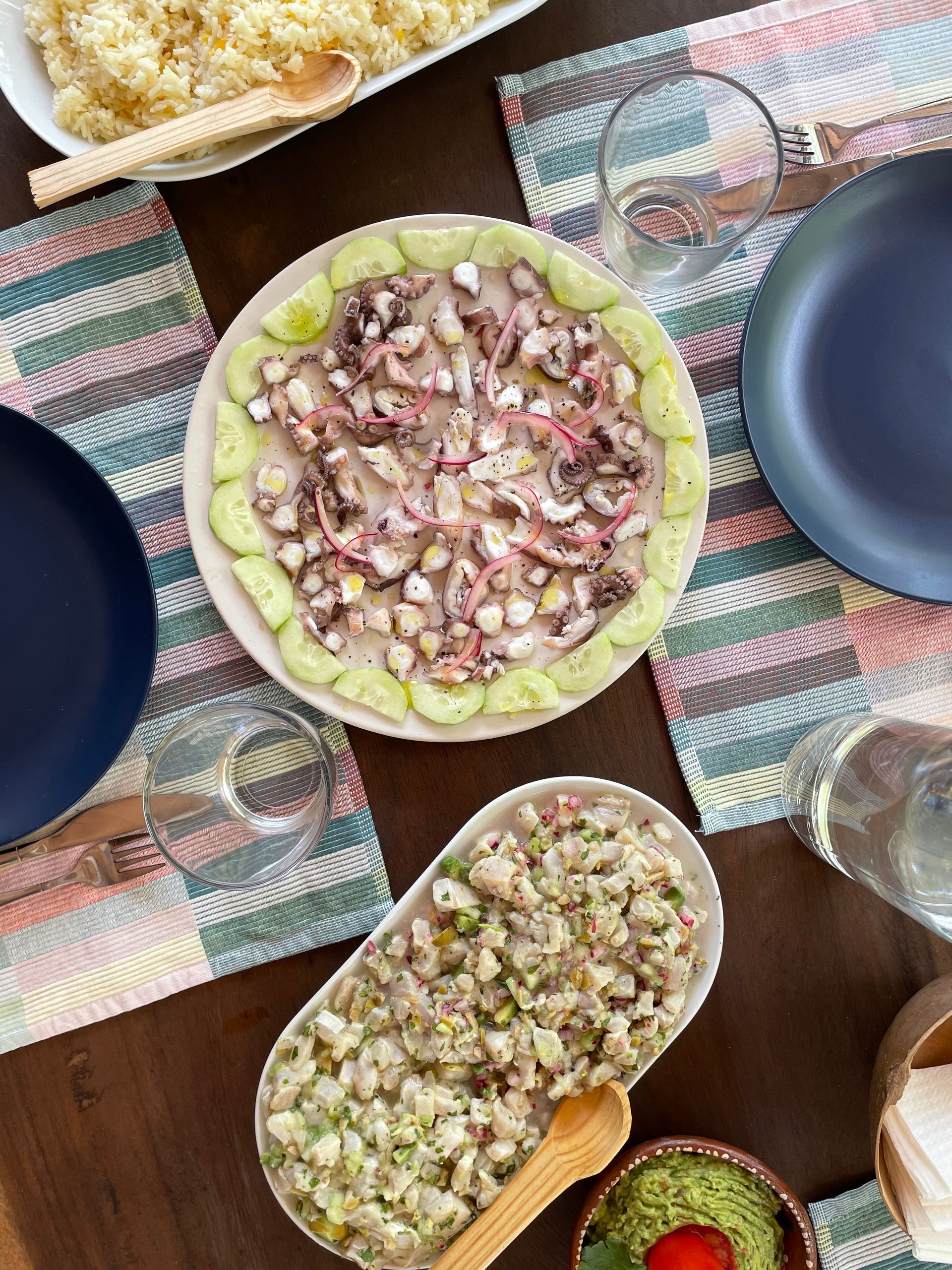 Overhead shot of a table set for a meal featuring ceviche and octopus salad; place settings in blue and clear.