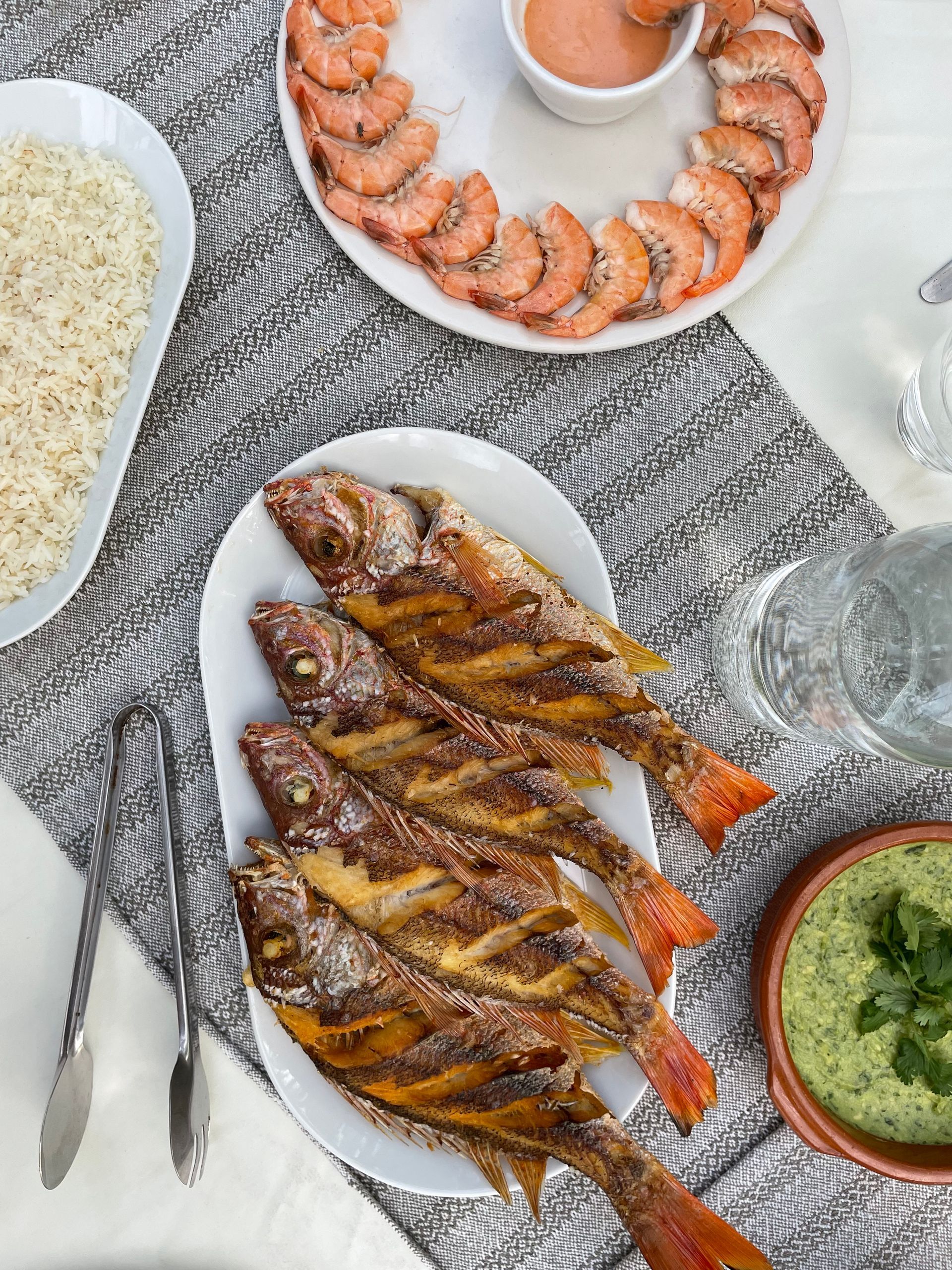 Grilled whole fish, shrimp, and sides on a table; overhead shot.