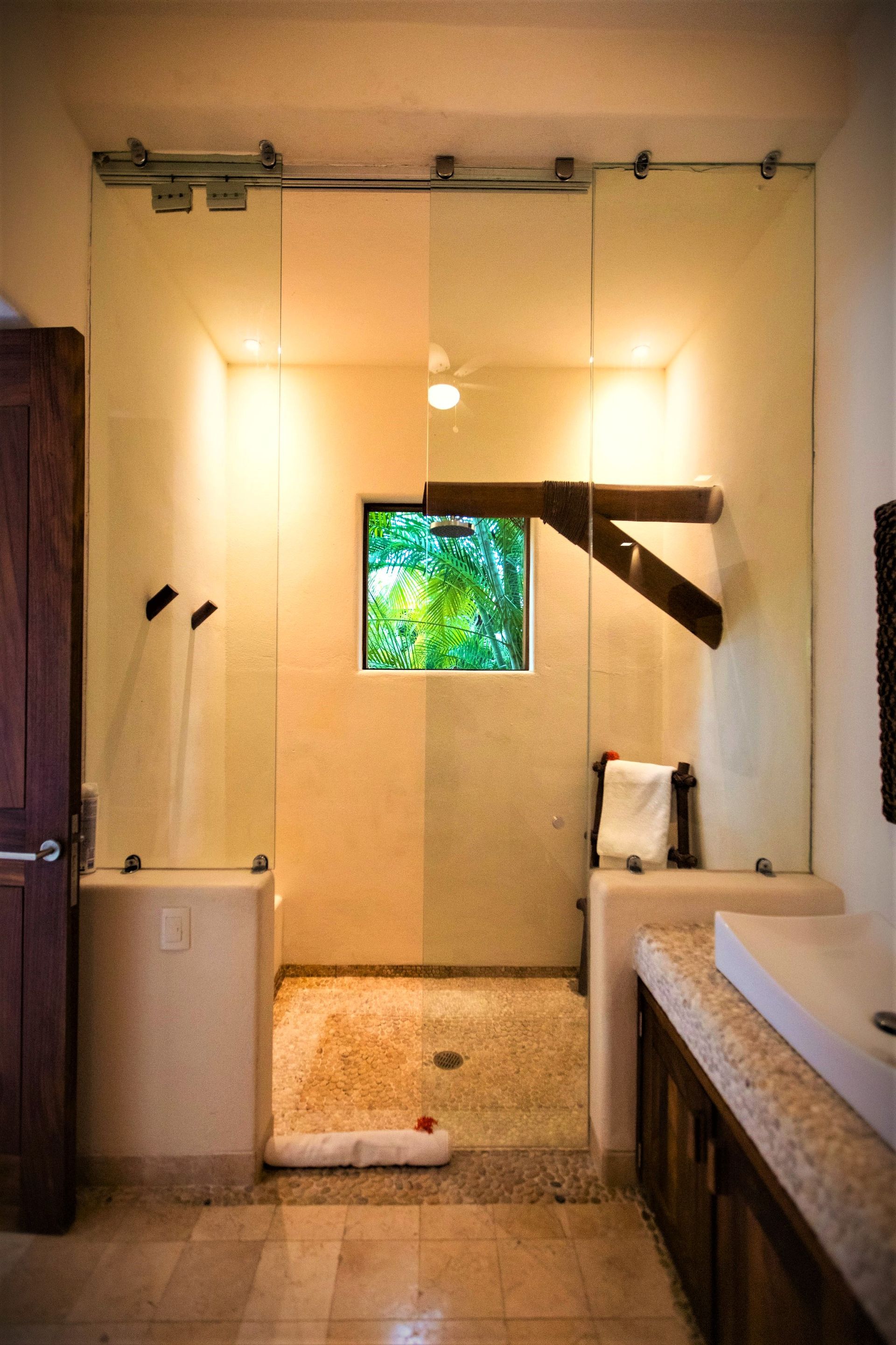 Ducha con puertas de cristal, paredes beige, una pequeña ventana y suelo de piedra.