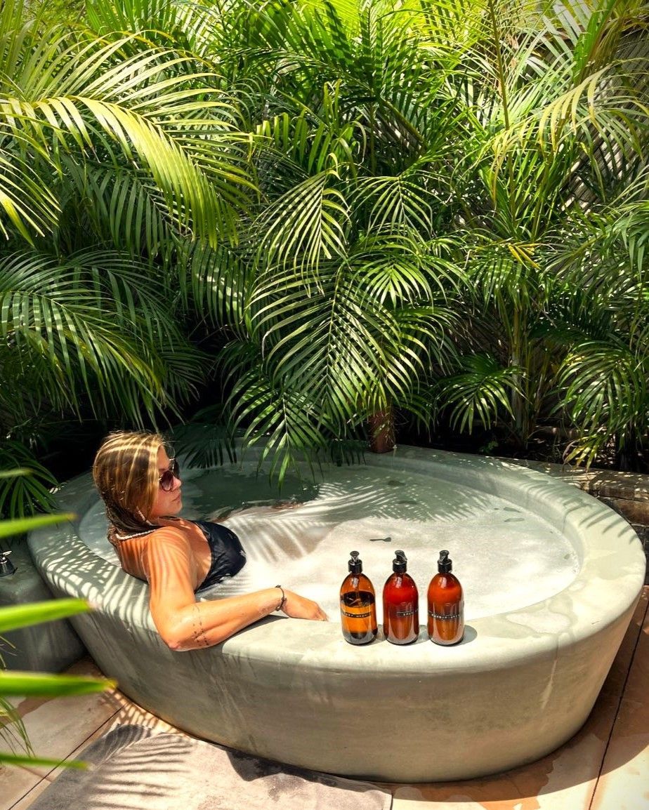 Woman in a hot tub with drinks, surrounded by tropical foliage.