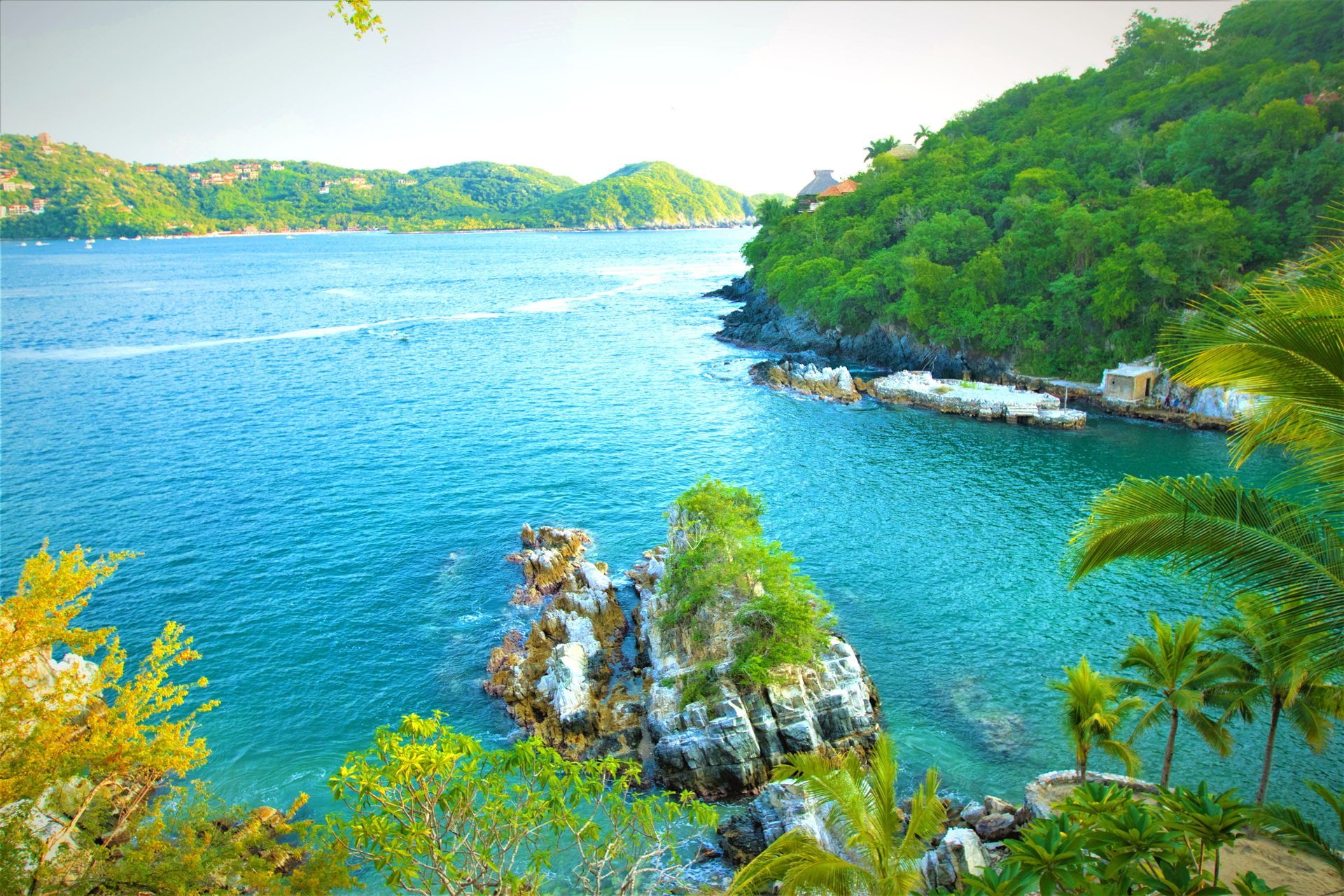 Vibrante vista costera: agua turquesa, exuberantes colinas verdes, afloramiento rocoso con vegetación.