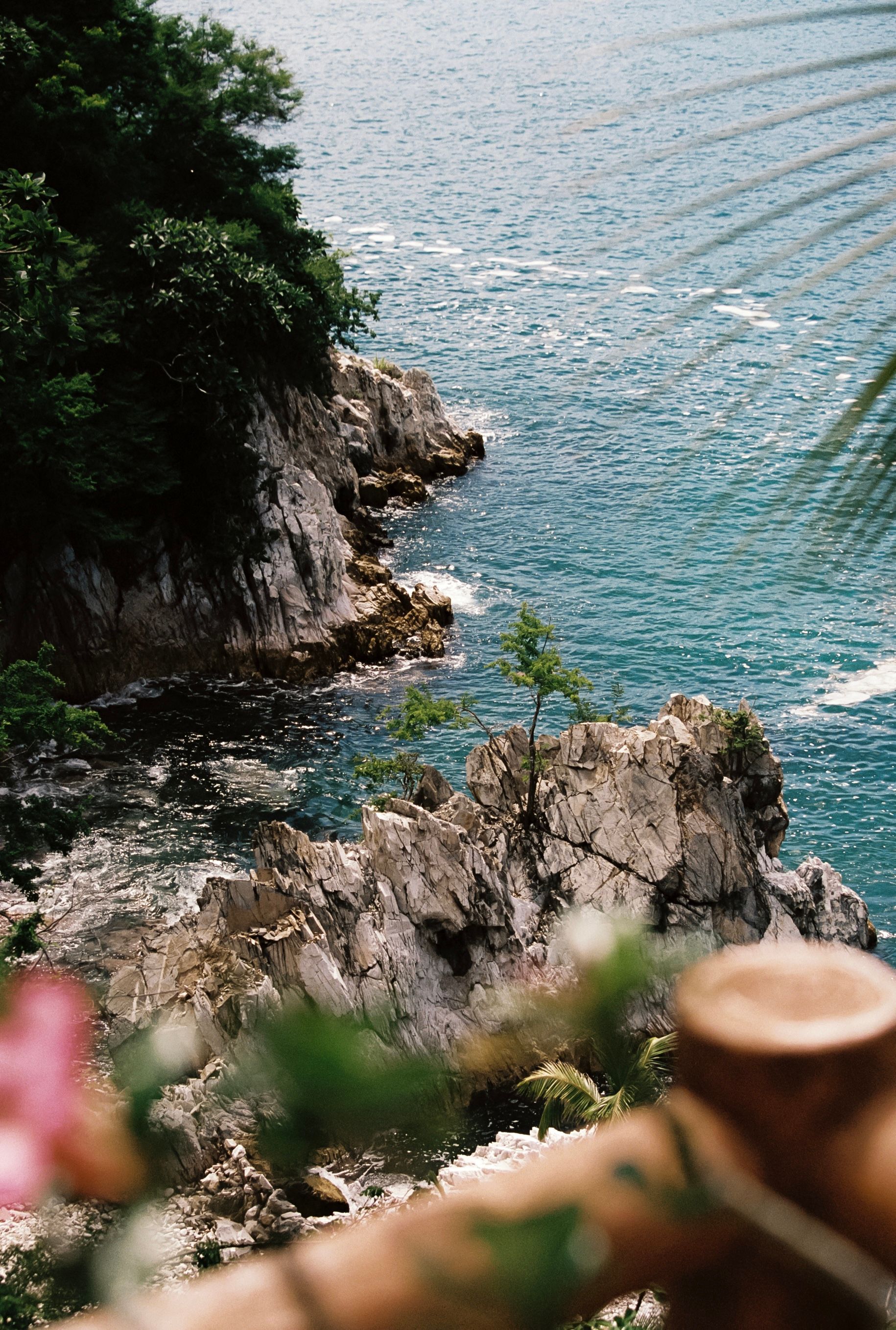 Costa rocosa con aguas turquesas. Árboles y arbustos verdes en las rocas. Valla de madera en primer plano.