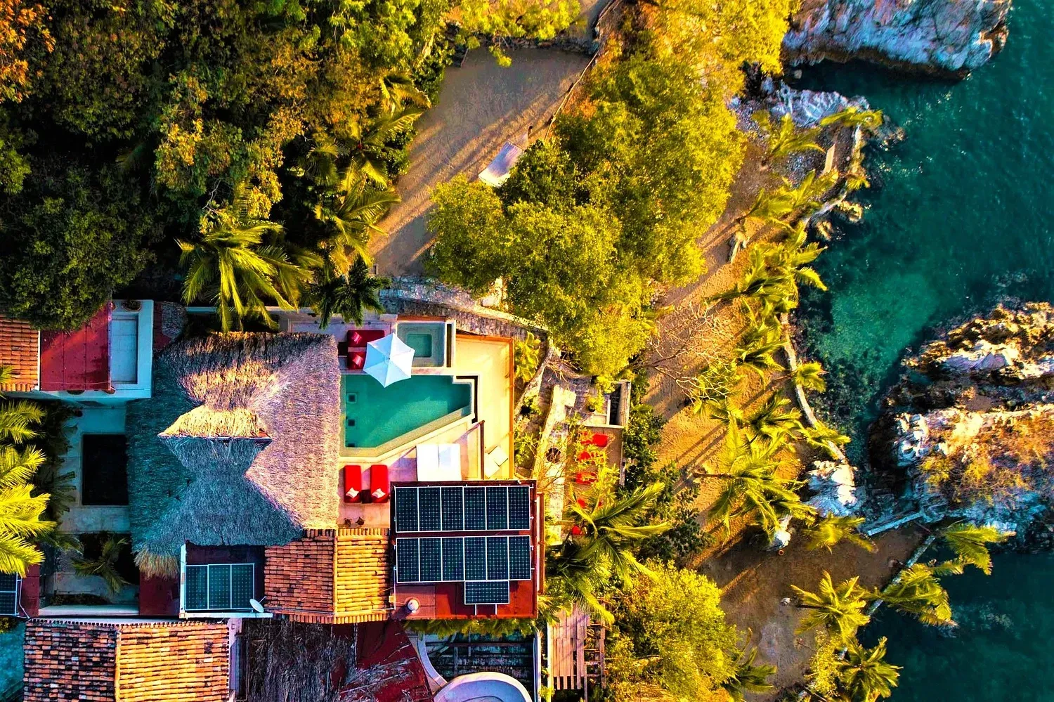 Vista aérea de una villa tropical con piscina, océano y exuberante vegetación.