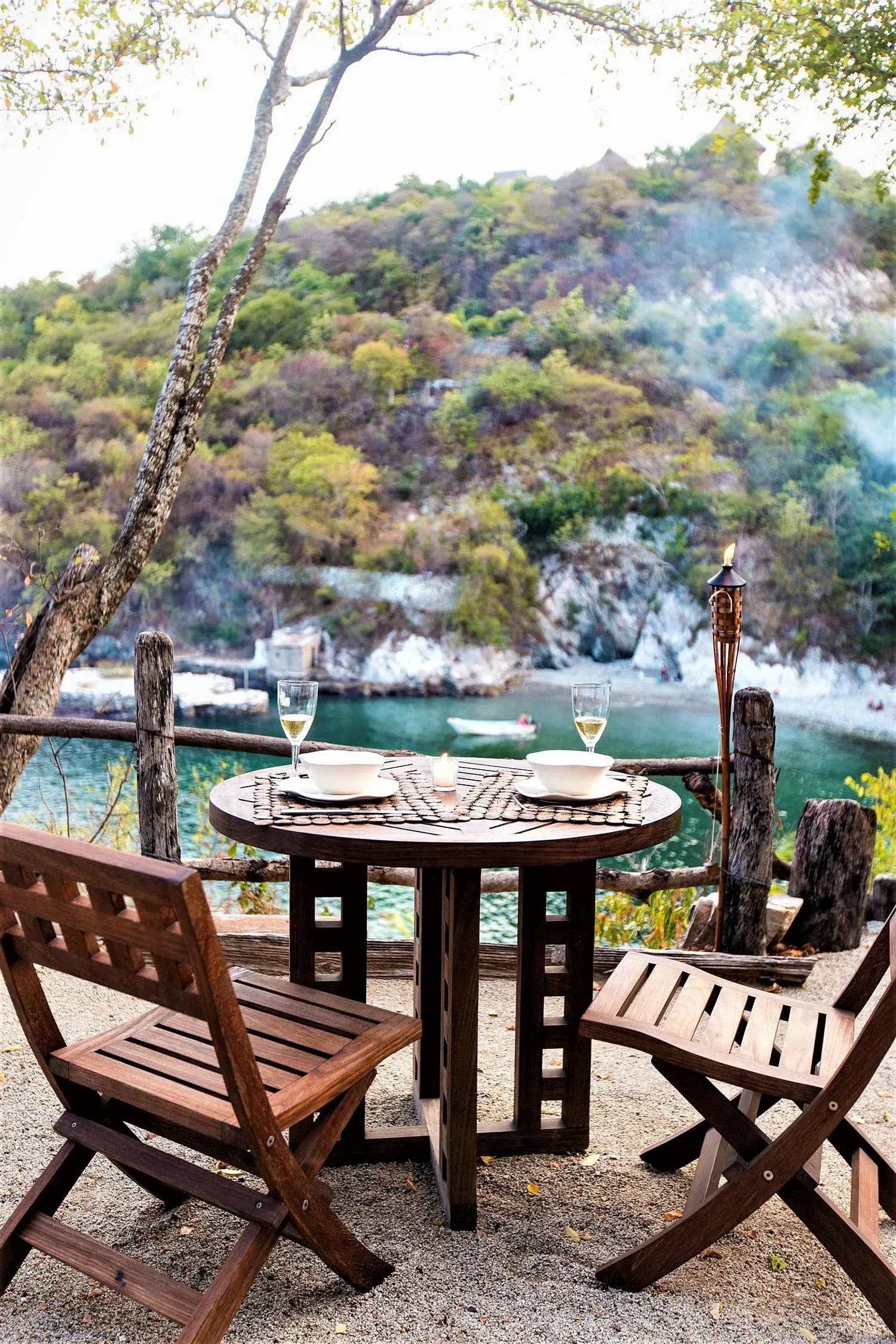 Juego de mesa y sillas de madera para dos con vista a un pintoresco lago con un fondo montañoso.