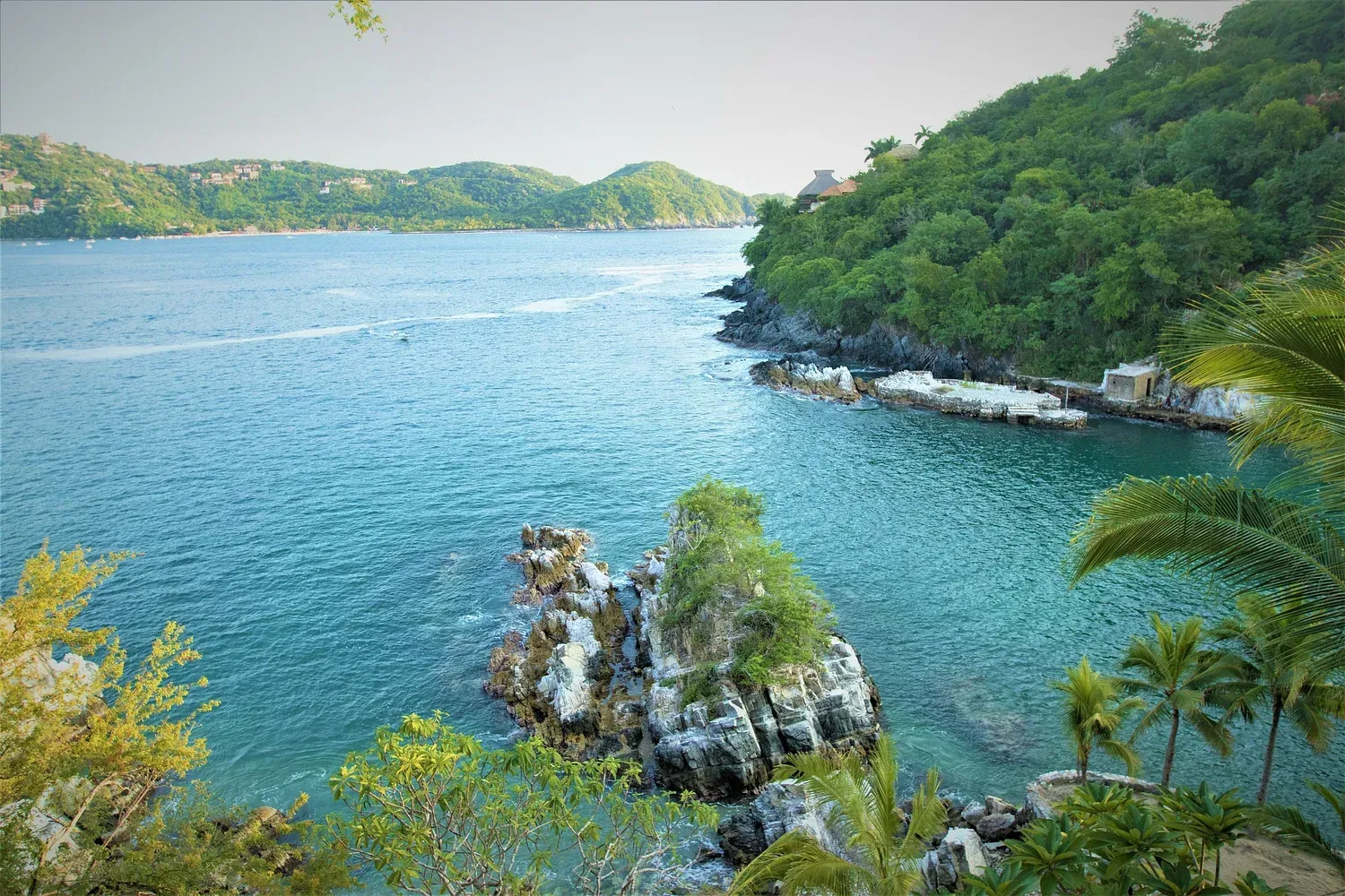 Bahía de aguas turquesas y exuberantes acantilados verdes.