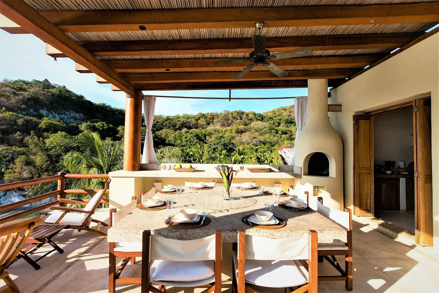 Comedor al aire libre con mesa puesta para invitados, con vista a un exuberante paisaje verde.