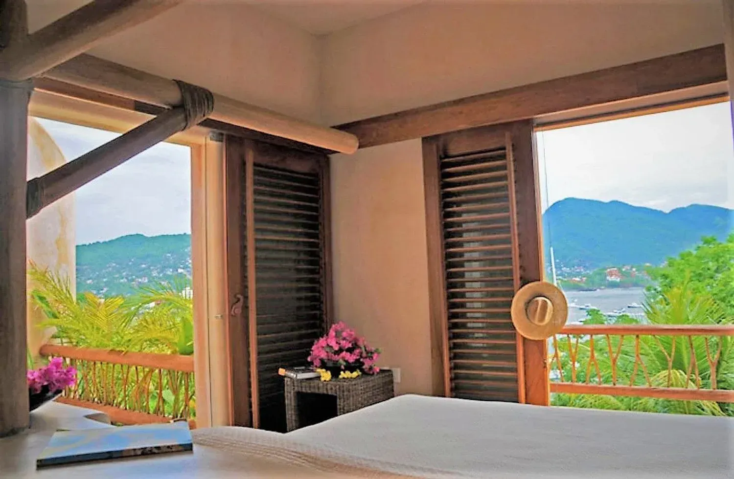 Dormitorio con vista al mar, vigas de madera, persianas, sombrero y flores.