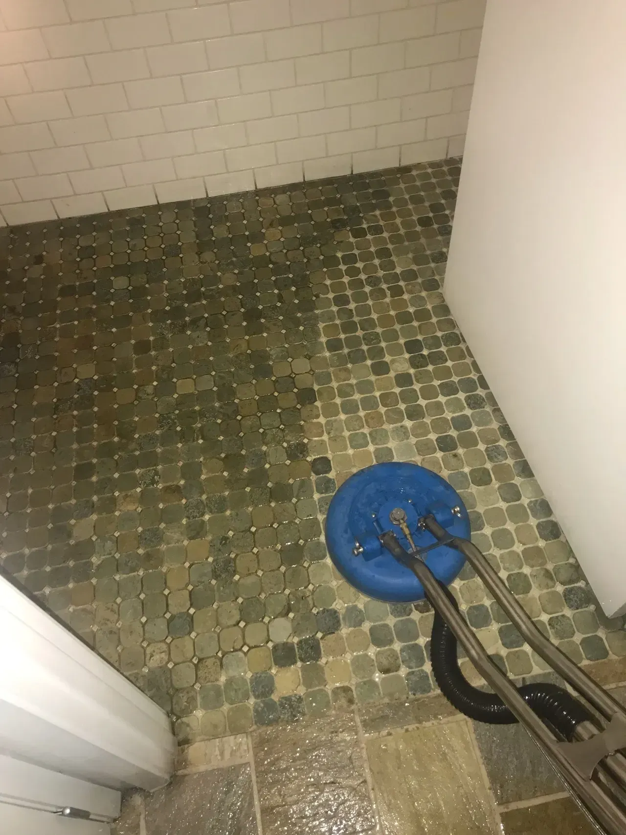 Blue floor cleaning machine on a tiled bathroom floor. White wall and door frame.