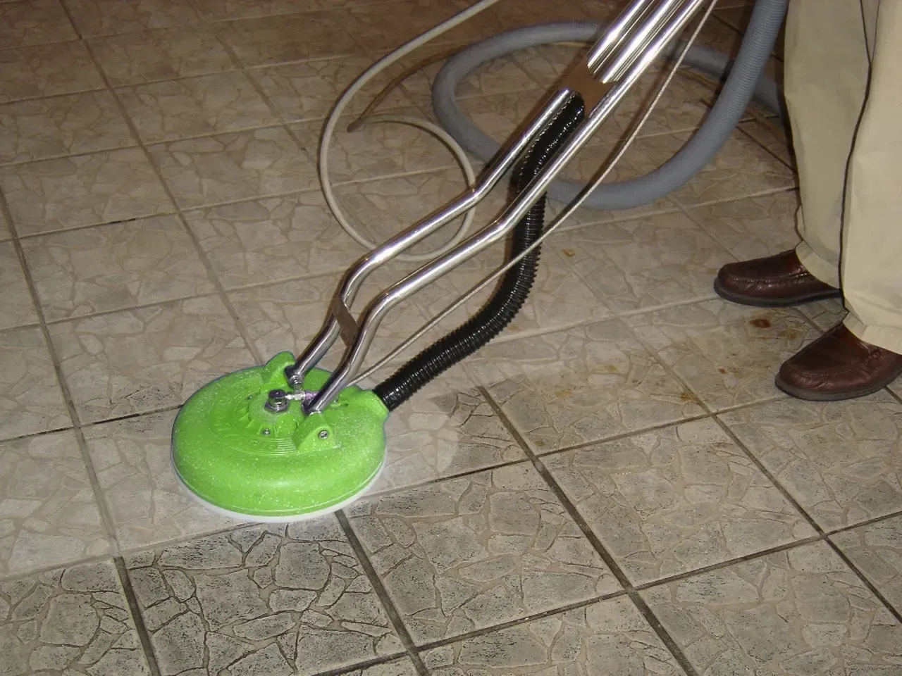 Person cleaning tile floor with green circular cleaning machine.