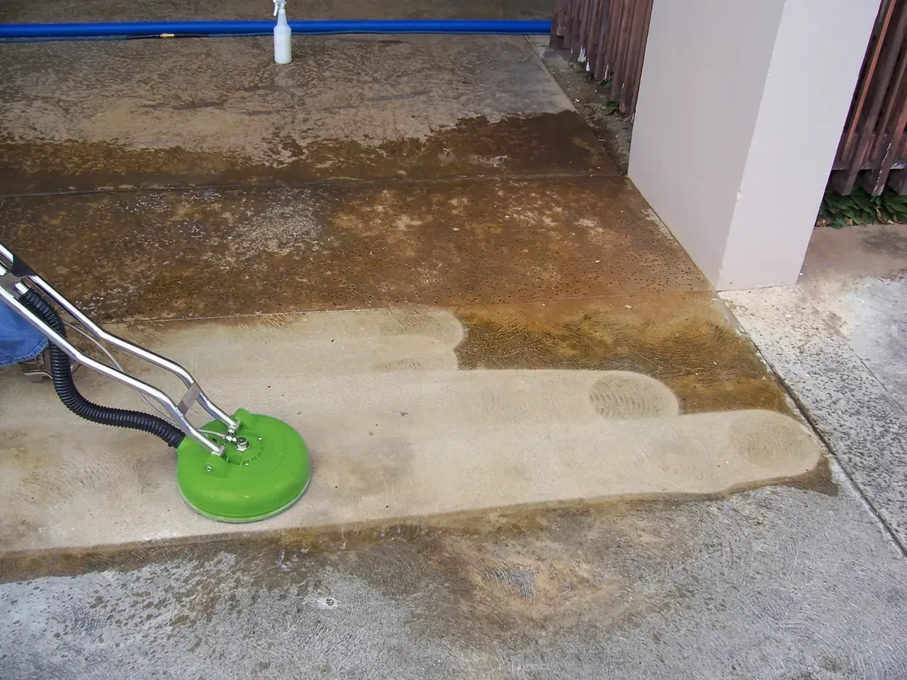 Power washer cleaning a concrete surface, leaving clean patches and dirty residue.