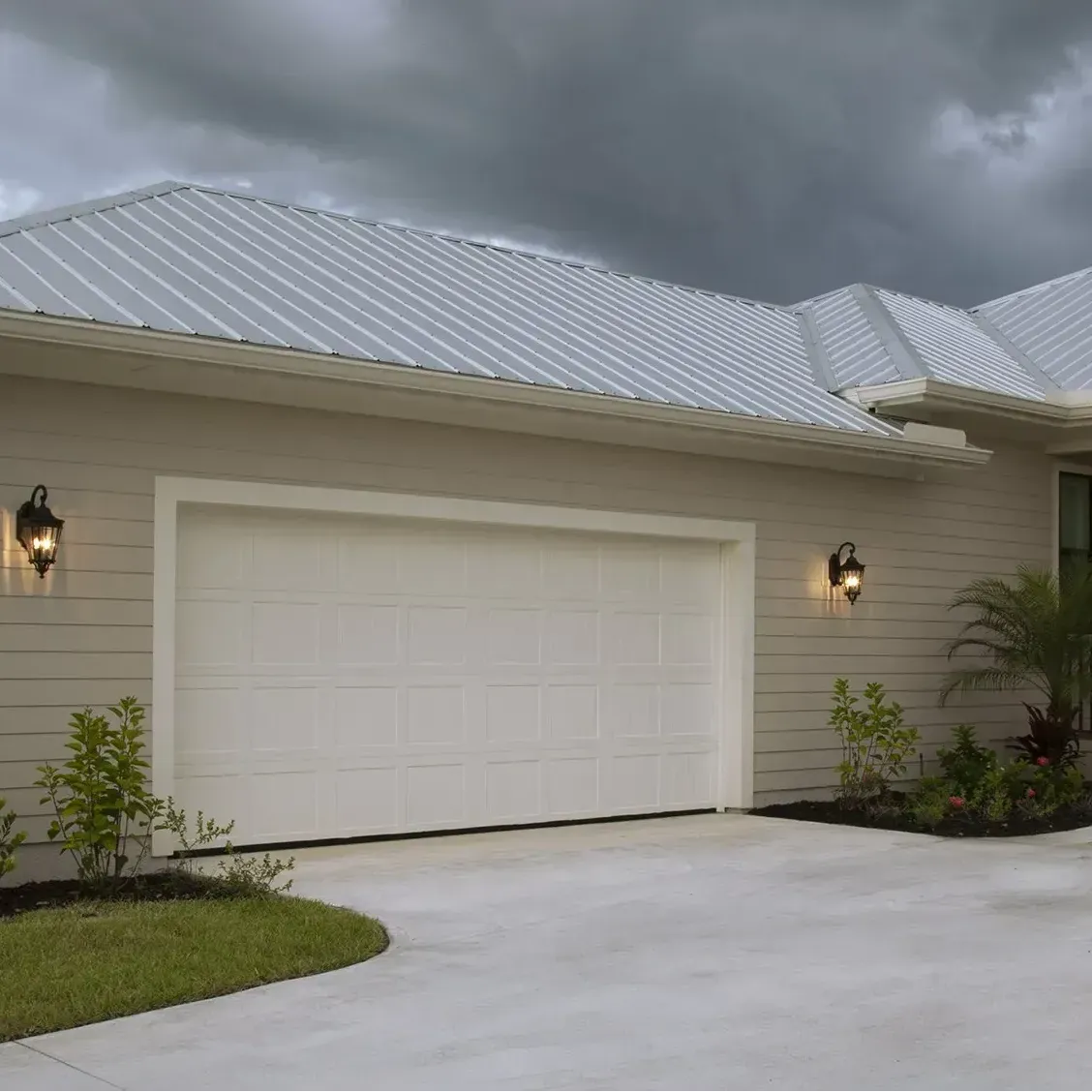 White garage door on beige house with metal roof; driveway and landscaping.