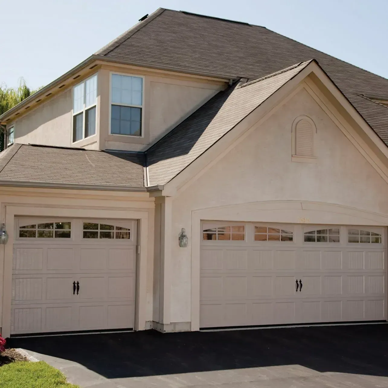 Two beige garage doors on a light-colored house.  One with an arched window design.