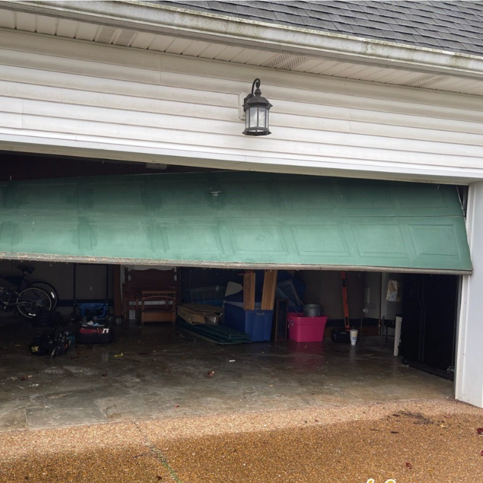 Green garage door partially open, revealing a cluttered garage interior.