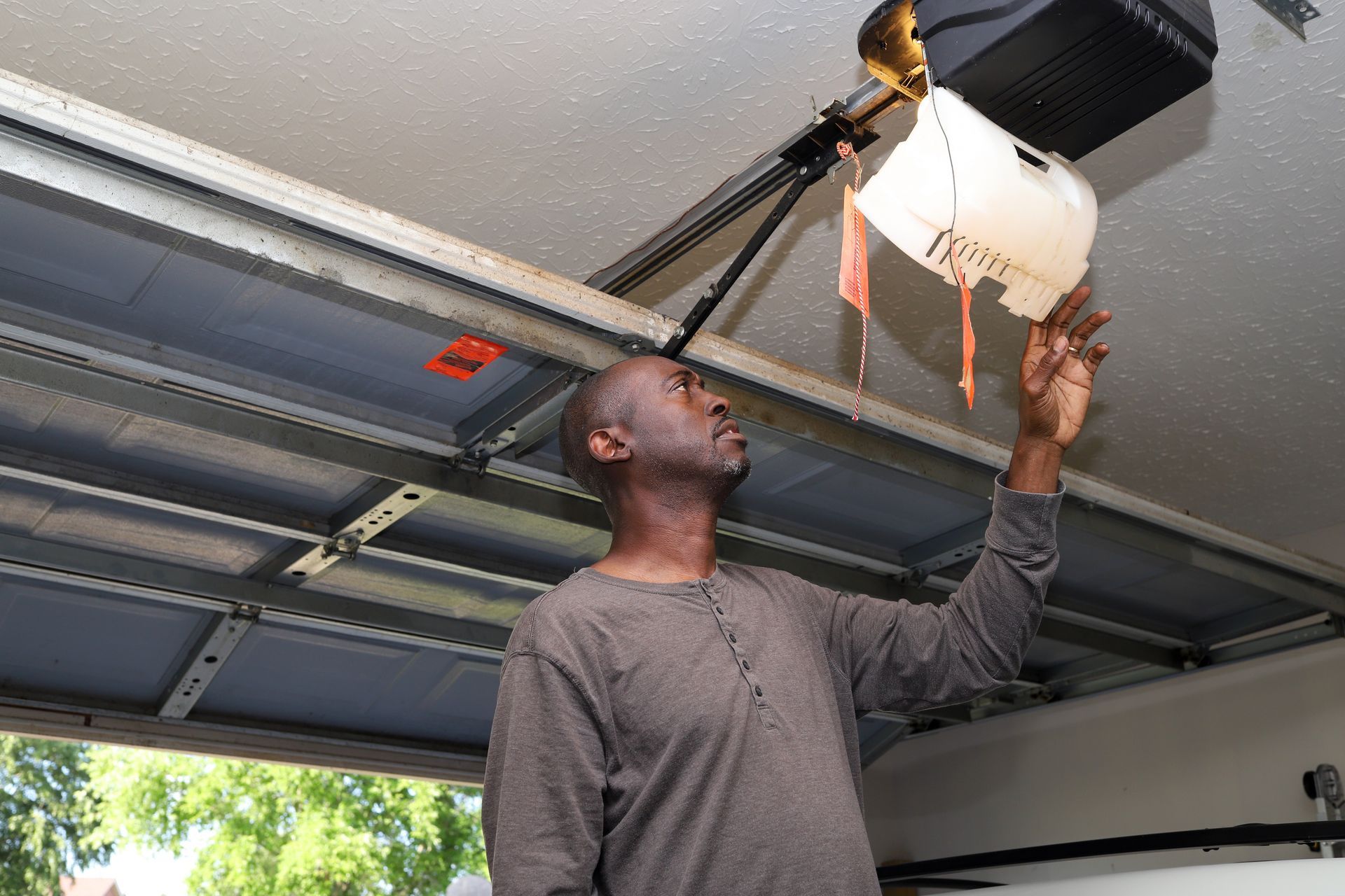 Man looking up, pouring liquid from a container near a garage door opener.