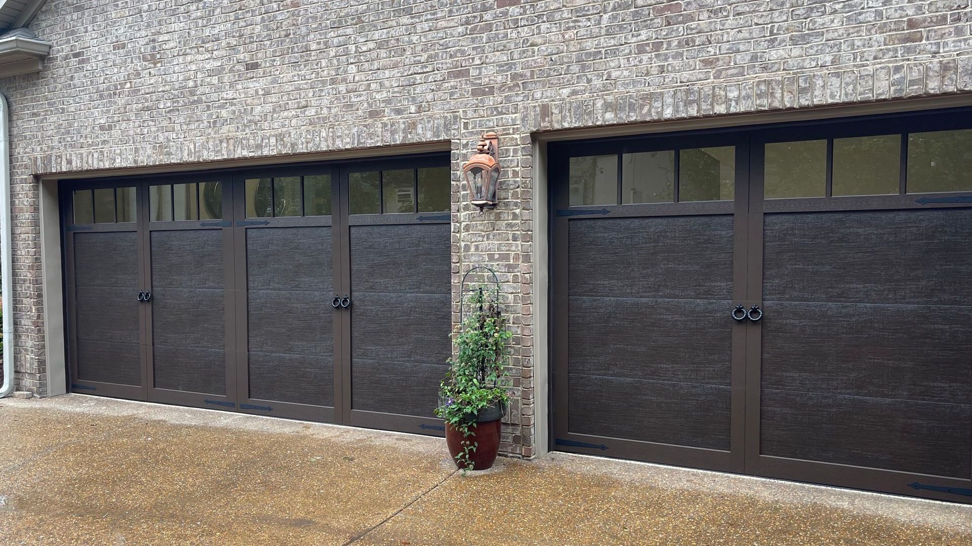 A row of garage doors on a brick building with a potted plant in front of them.
