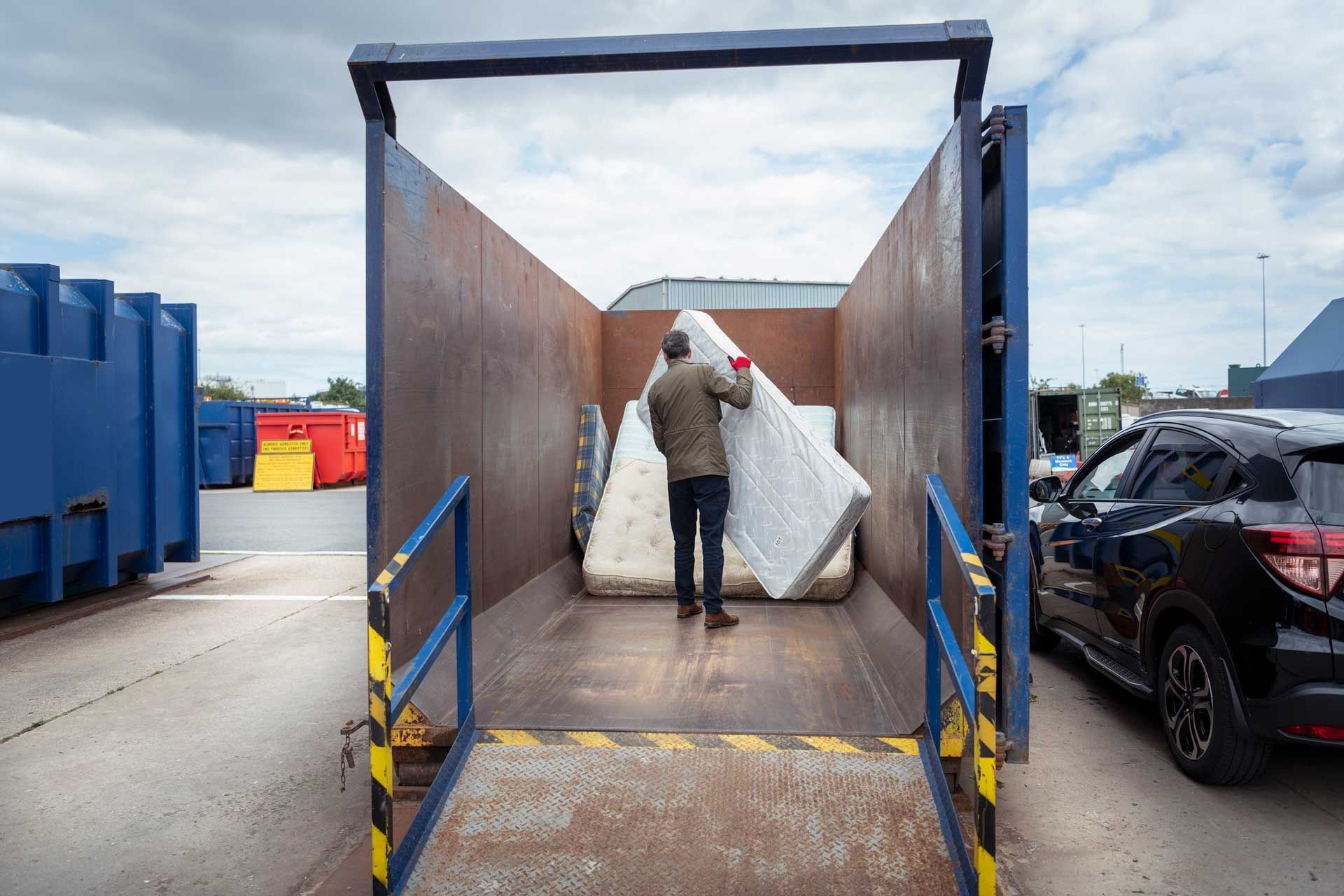 A man is loading a mattress into a dumpster.